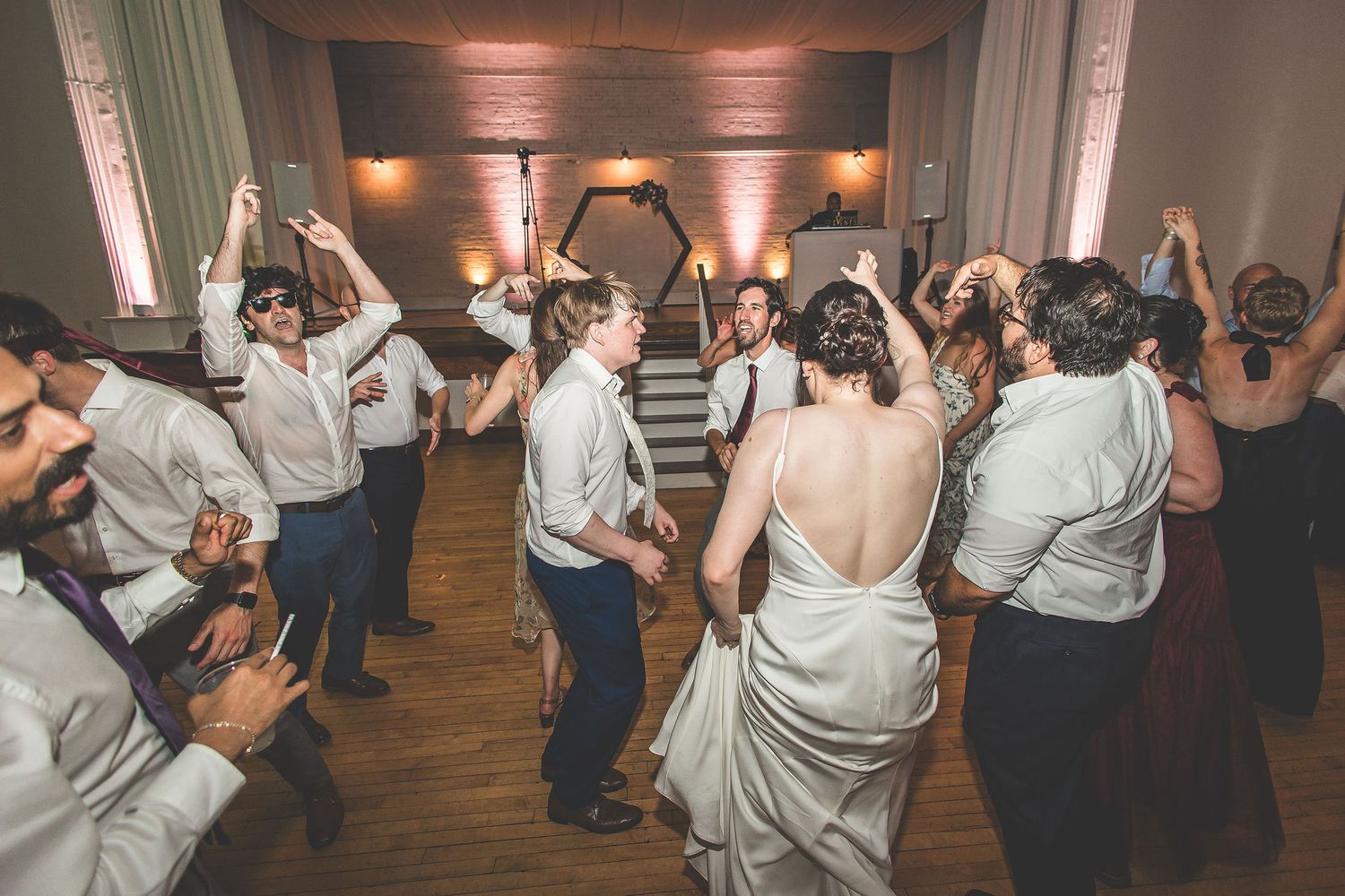 Wedding guests dancing and celebrating on a wooden dance floor with dramatic lighting effects.