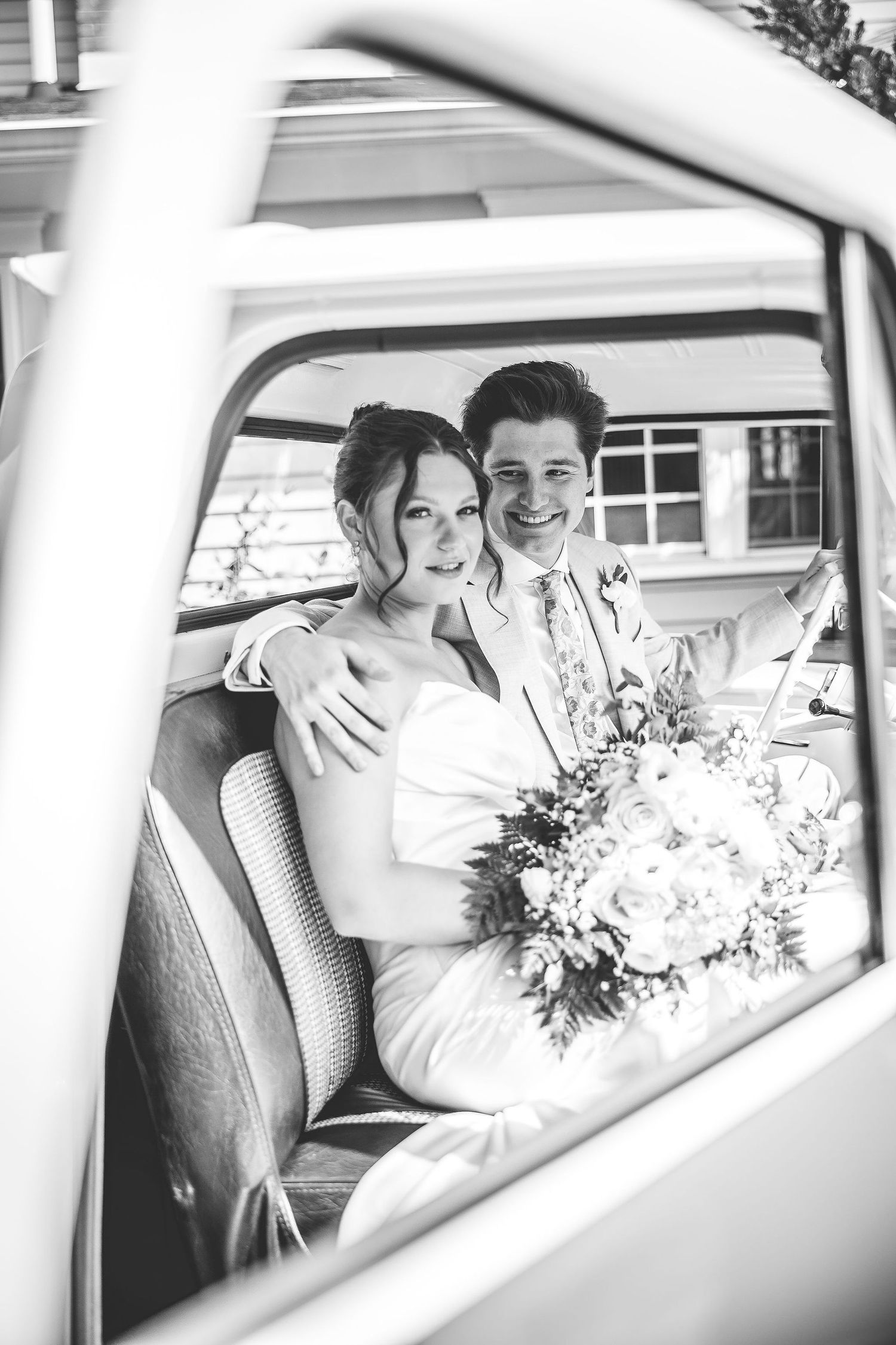 Black and white wedding photos taken through vintage car windows with floral bouquet visible.