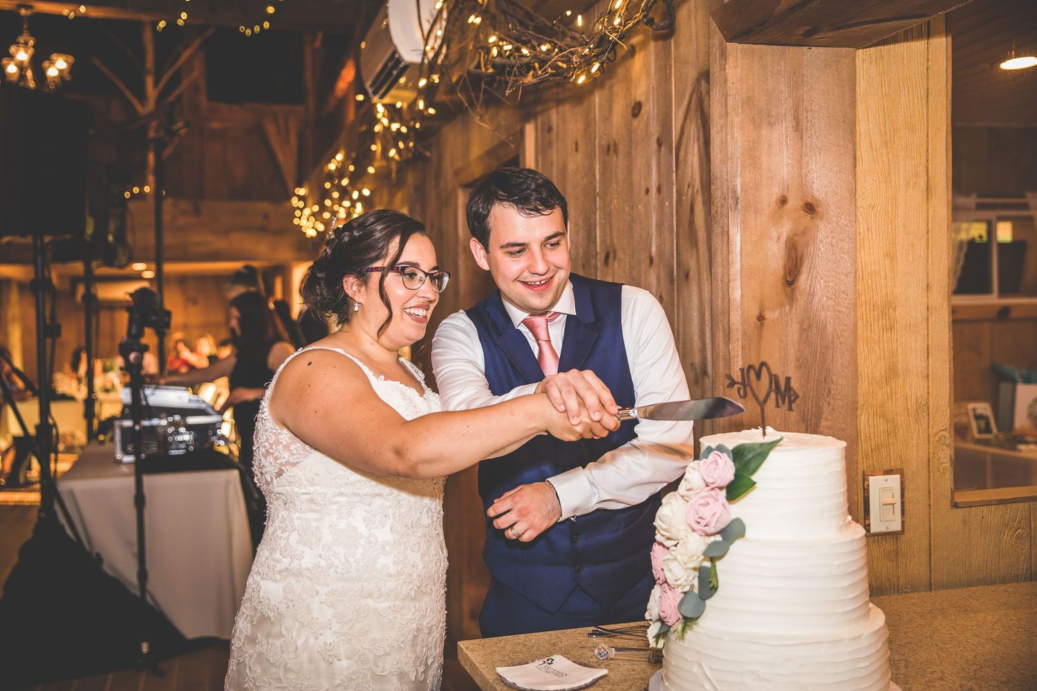 Bride and groom share cake cutting moment at rustic barn wedding reception.