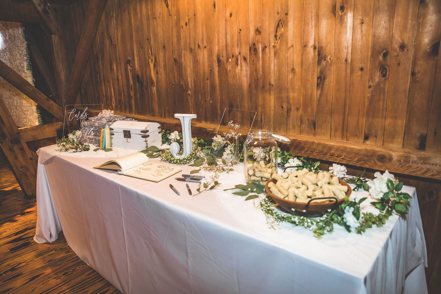 Long banquet table decorated with white linens and floral arrangements in rustic wooden interior.