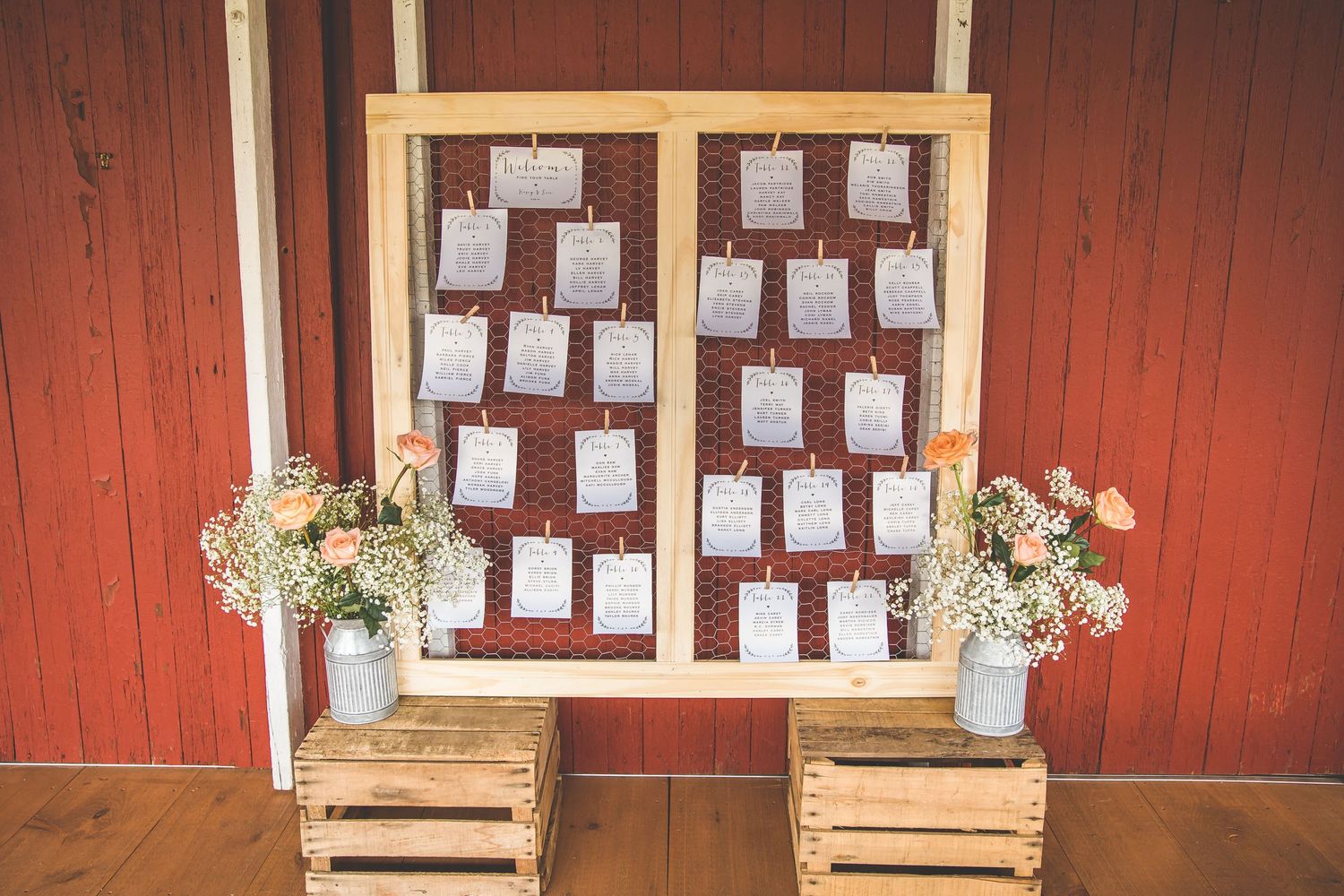 Rustic red barn wall with wooden frames displaying wedding seating arrangements.