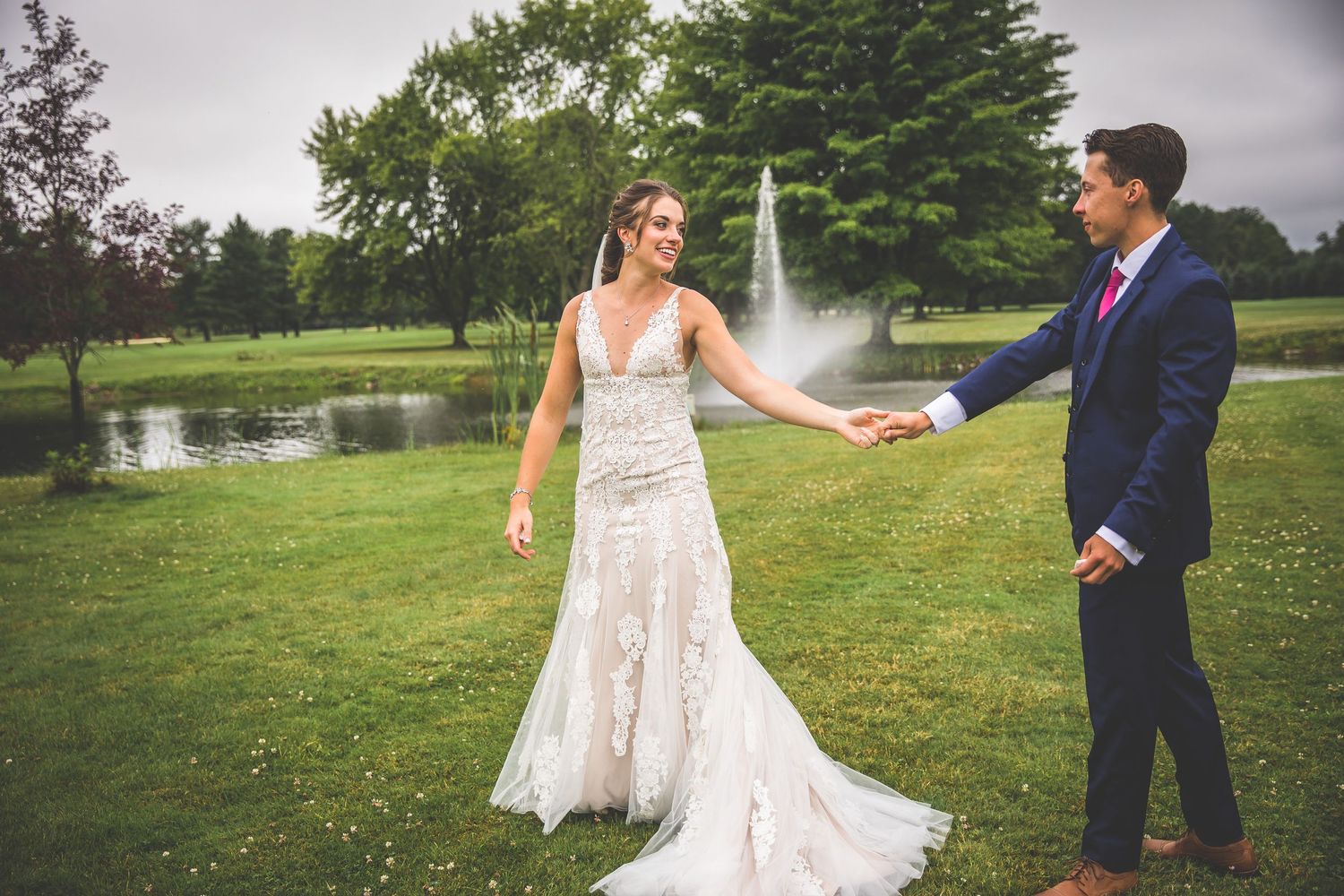 A beautiful wedding scene with a bride in lace gown reaching out on landscaped grounds.