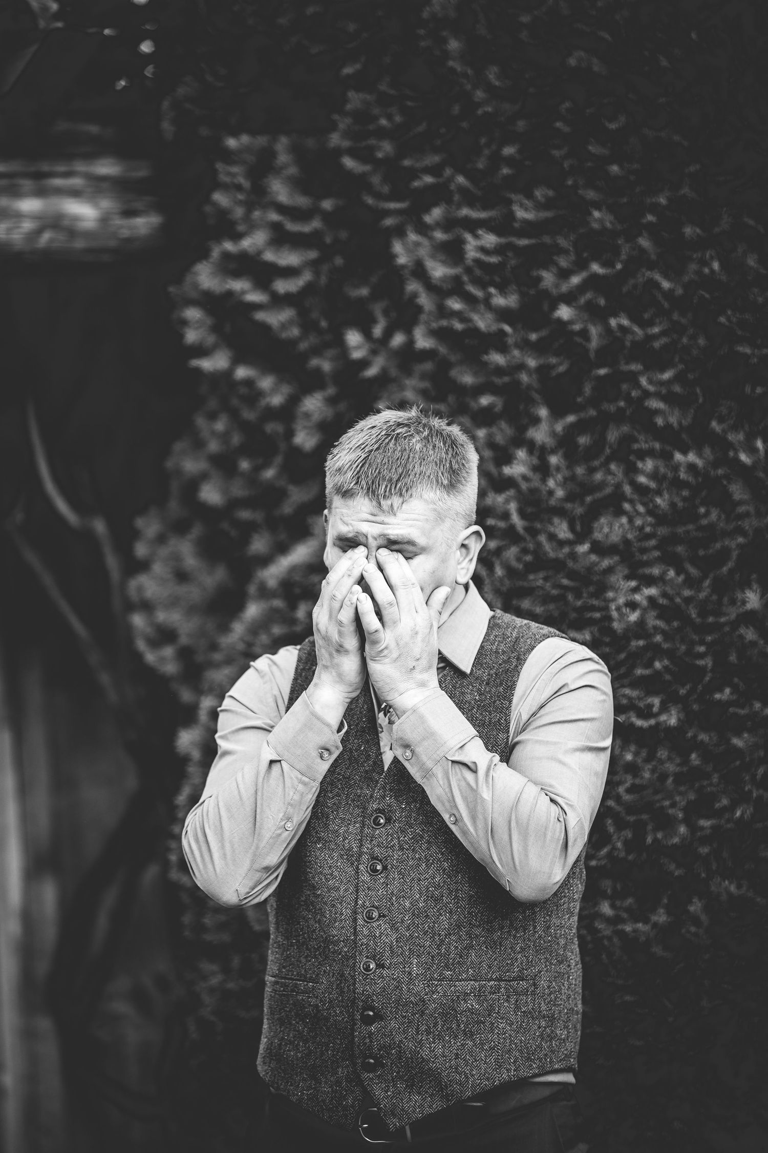Emotional black and white portrait of someone in a vest covering their face.