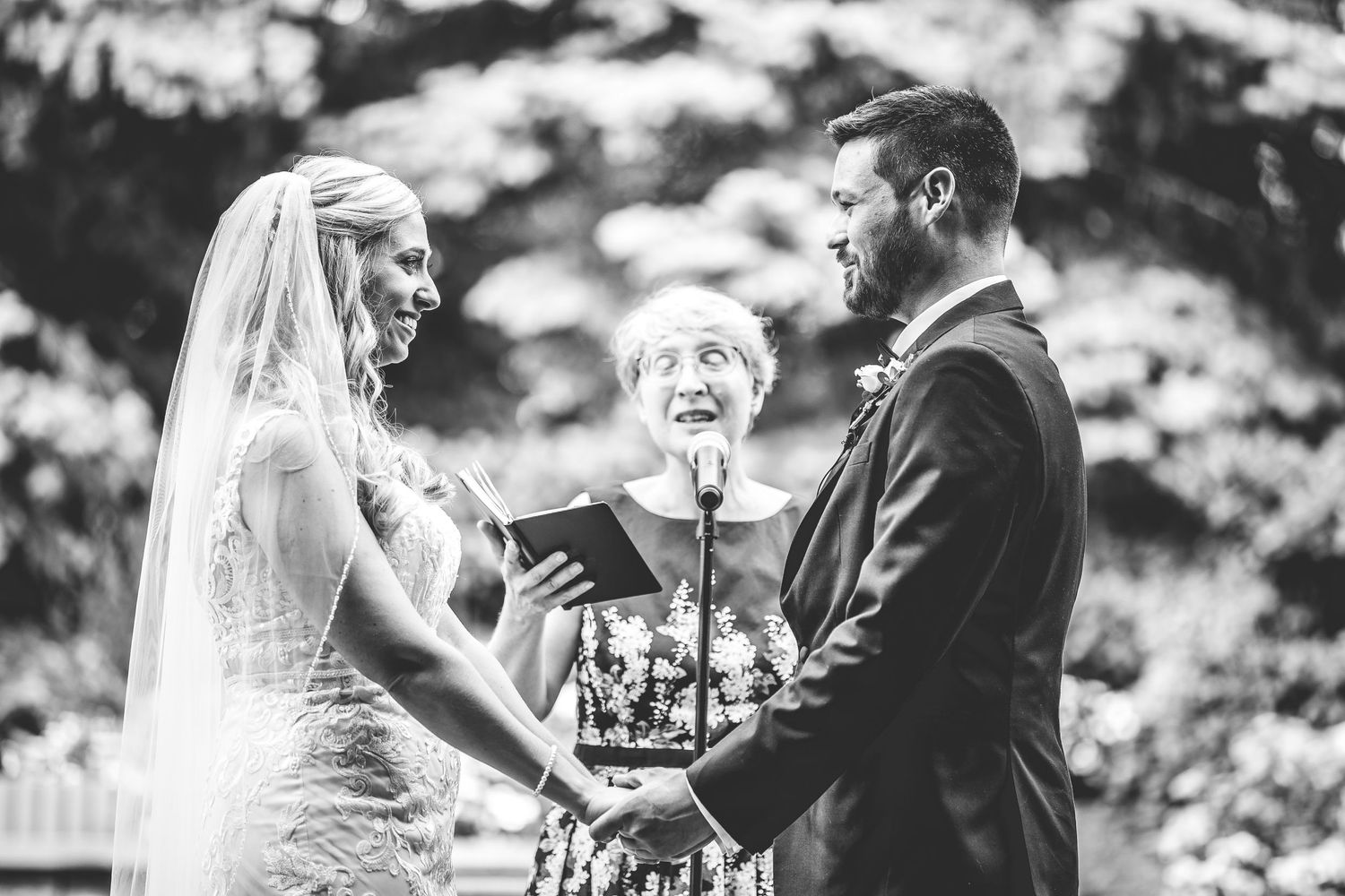 Black and white photo of wedding ceremony with couple exchanging vows outdoors.