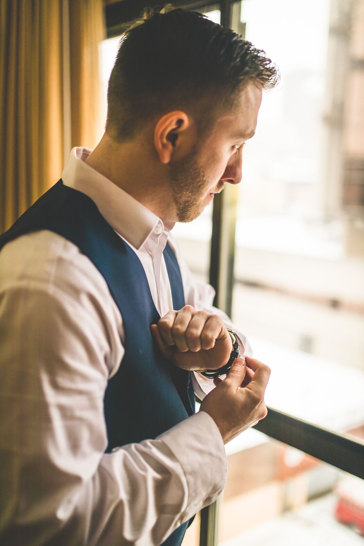 Side view of person adjusting formal attire near window.