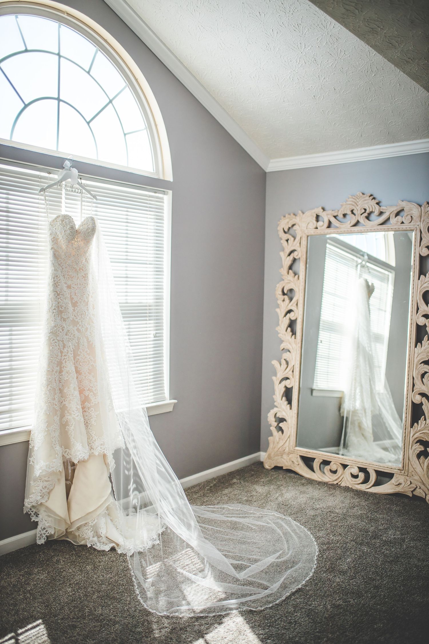 Elegant lace wedding dress displayed in front of arched windows with natural lighting.