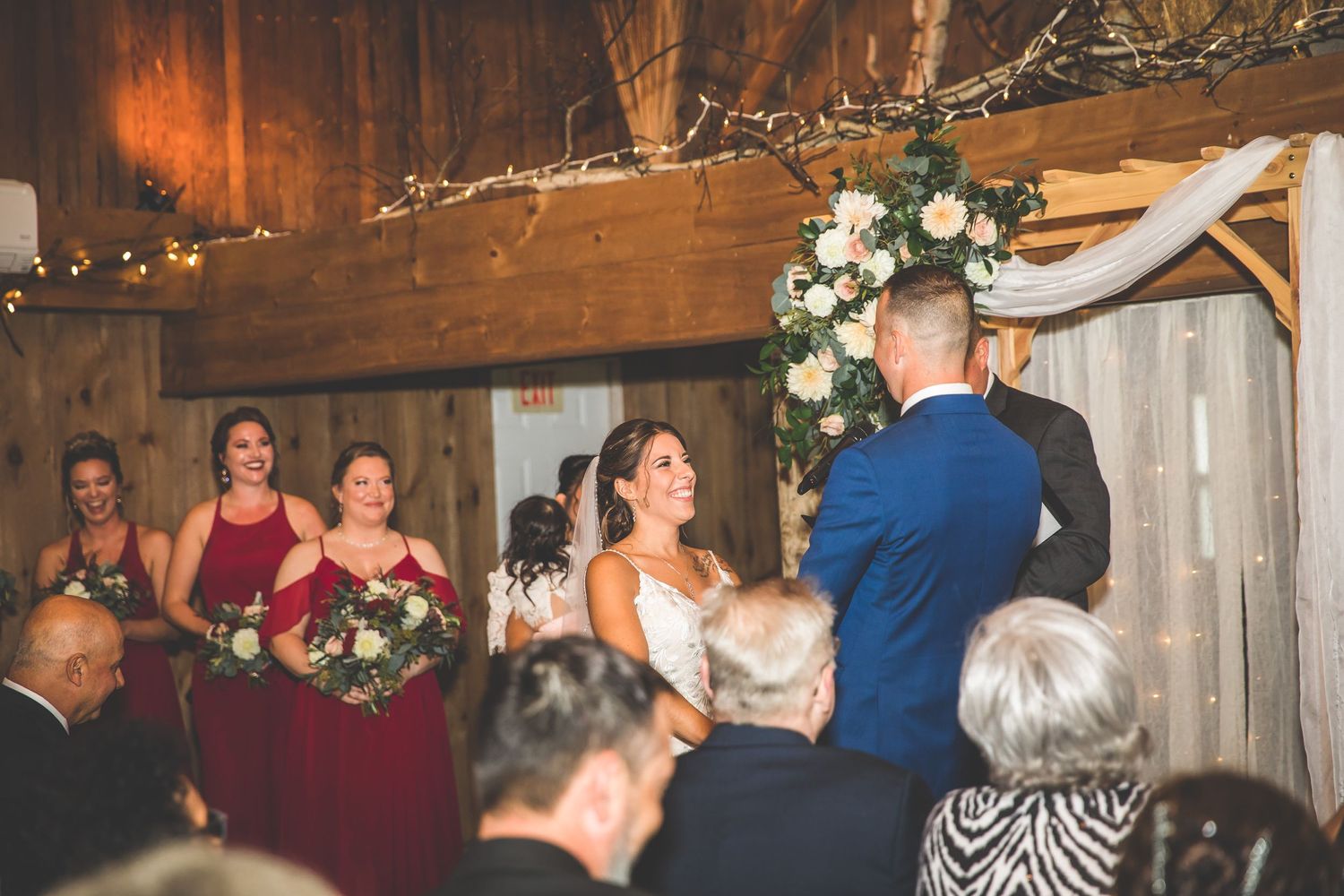 Wedding reception celebration in rustic barn venue with string lights and decorative branches.