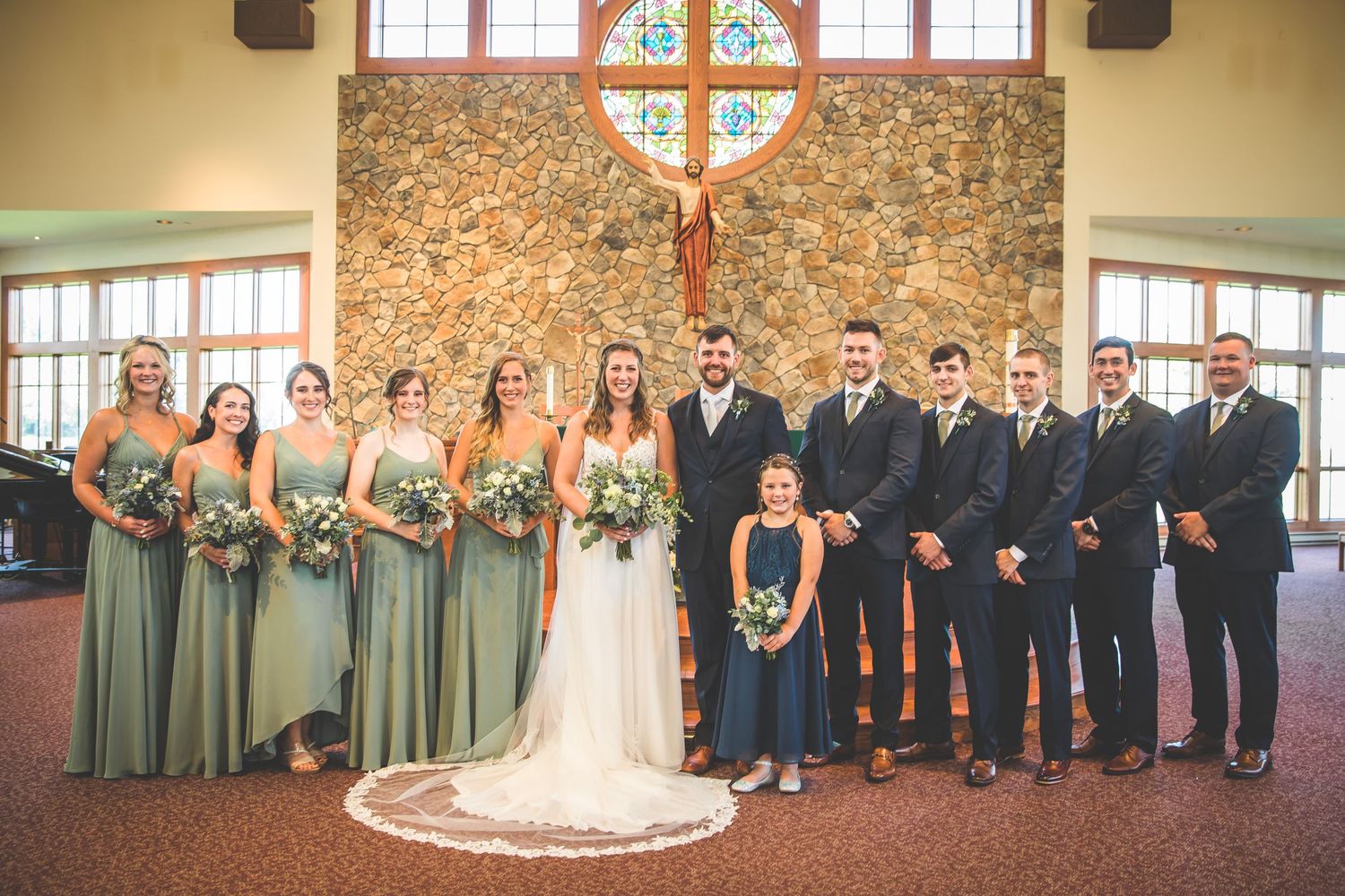 Full wedding party lineup with bridesmaids and groomsmen in a traditional church setting.
