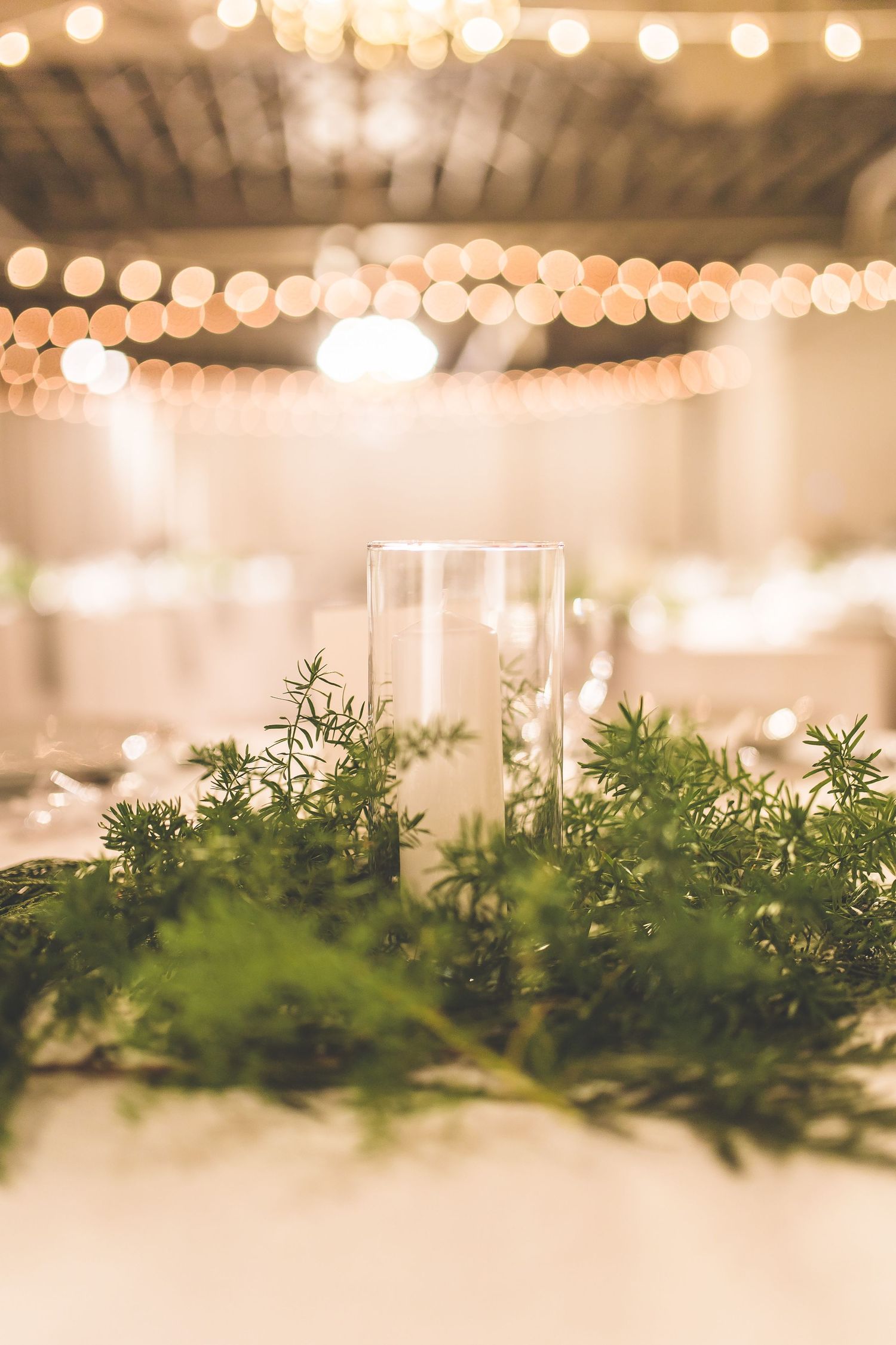 Elegant wedding reception table setting with greenery centerpiece and overhead string lights.