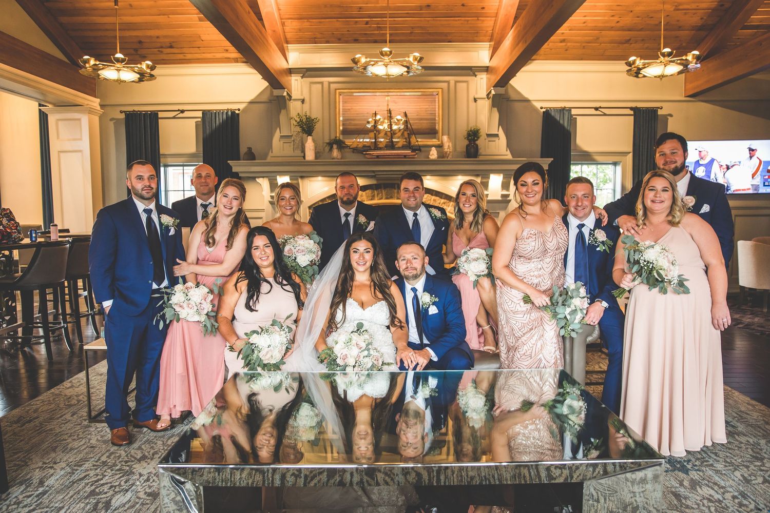Wedding party group photo in rustic venue with exposed wooden beams and ambient lighting.