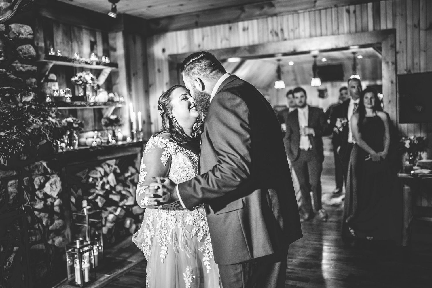 Wedding couple dances together in a rustic barn venue with wooden walls and ambient lighting.