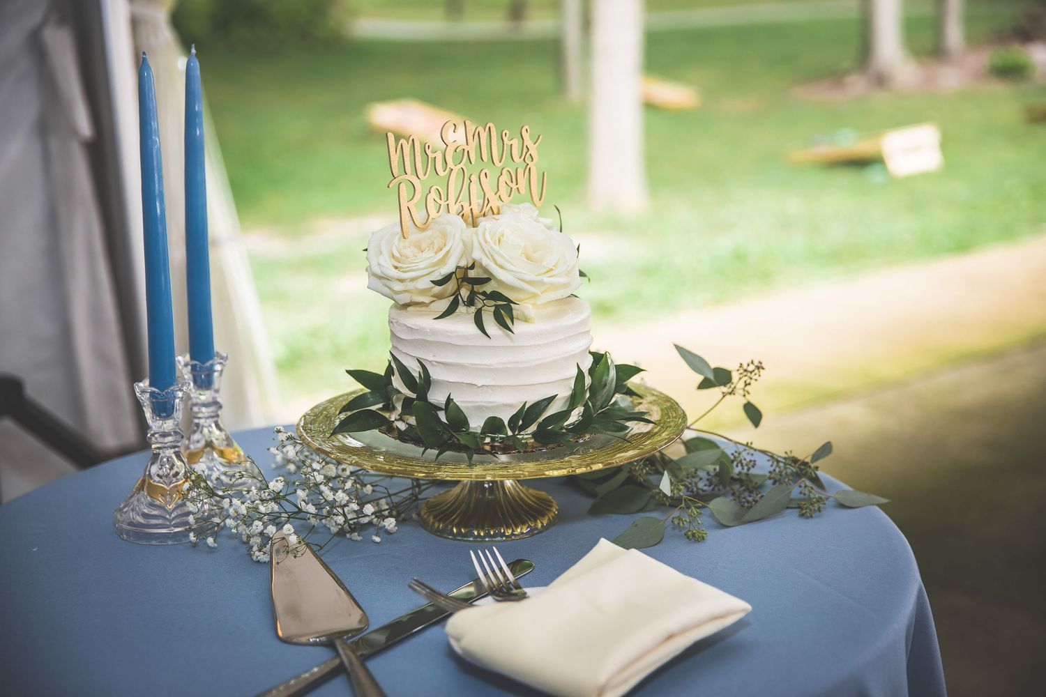 Wedding reception dessert table with white linens and greenery decorations.