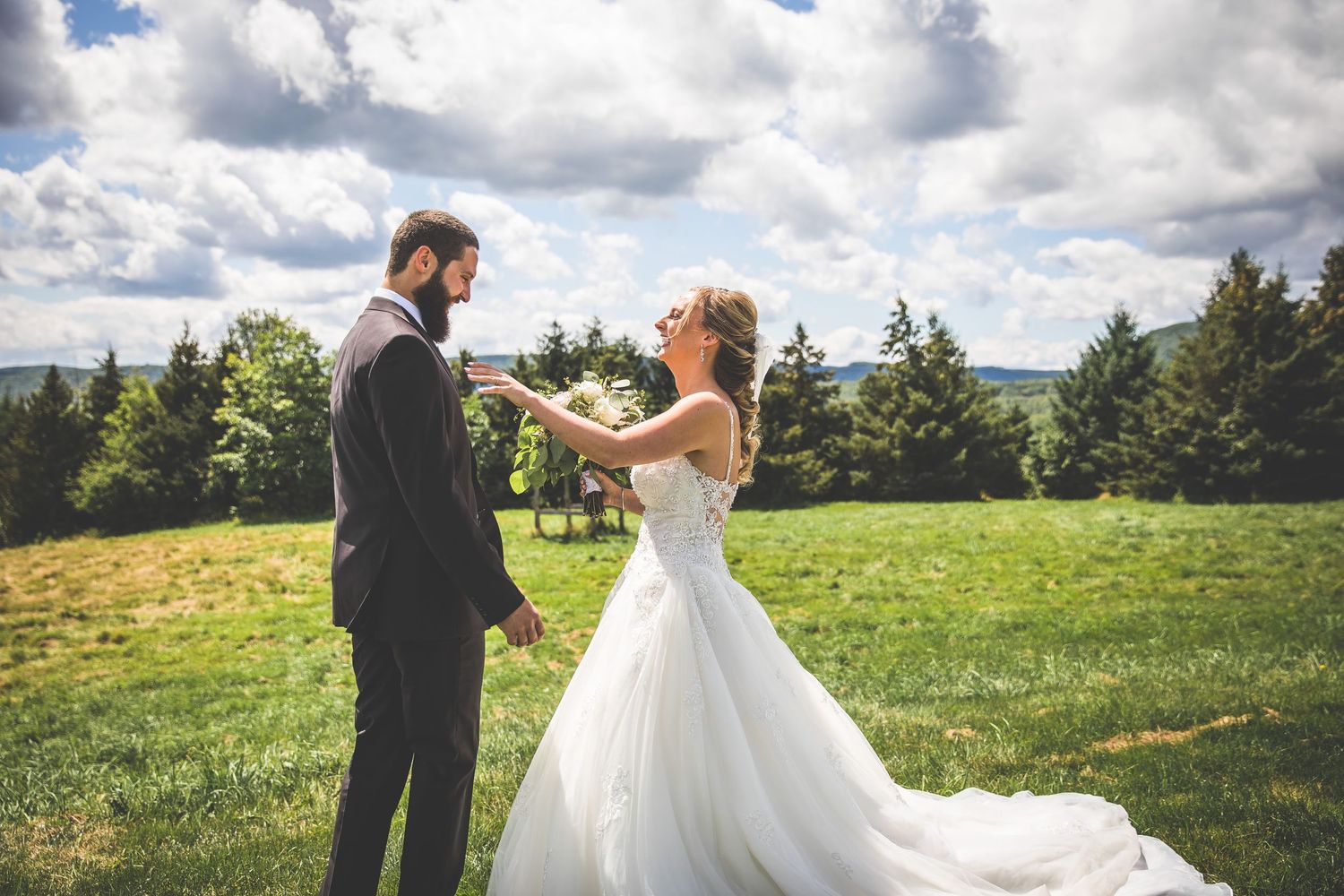 Bride and groom sharing intimate moment in sunny meadow with mountain backdrop.