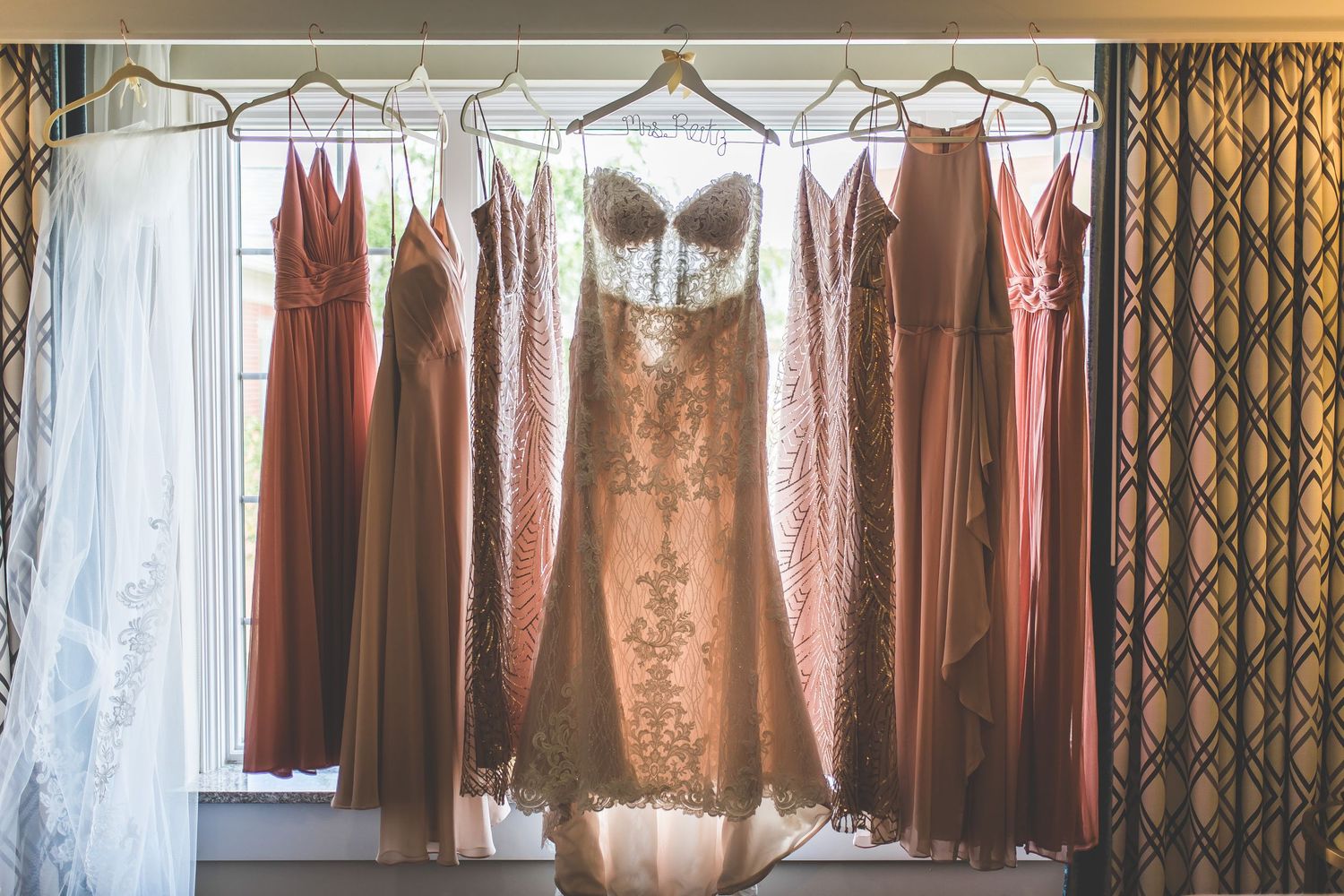 Row of rose gold and blush colored bridesmaid dresses hanging on display.