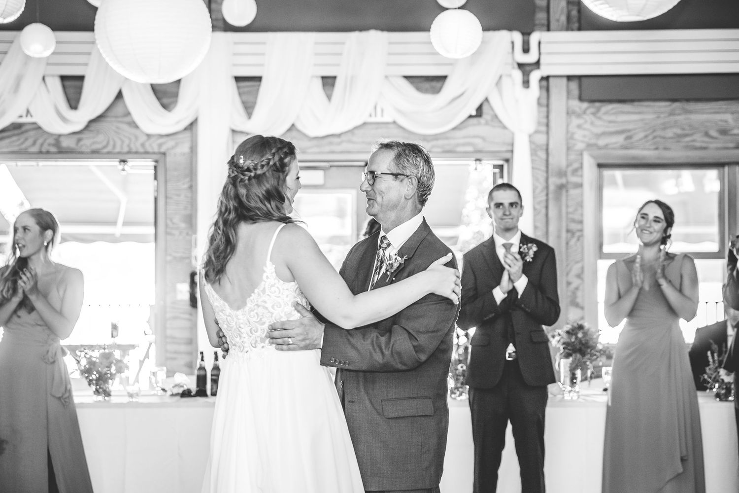 Wedding party members dancing and celebrating during reception with white paper lanterns overhead.