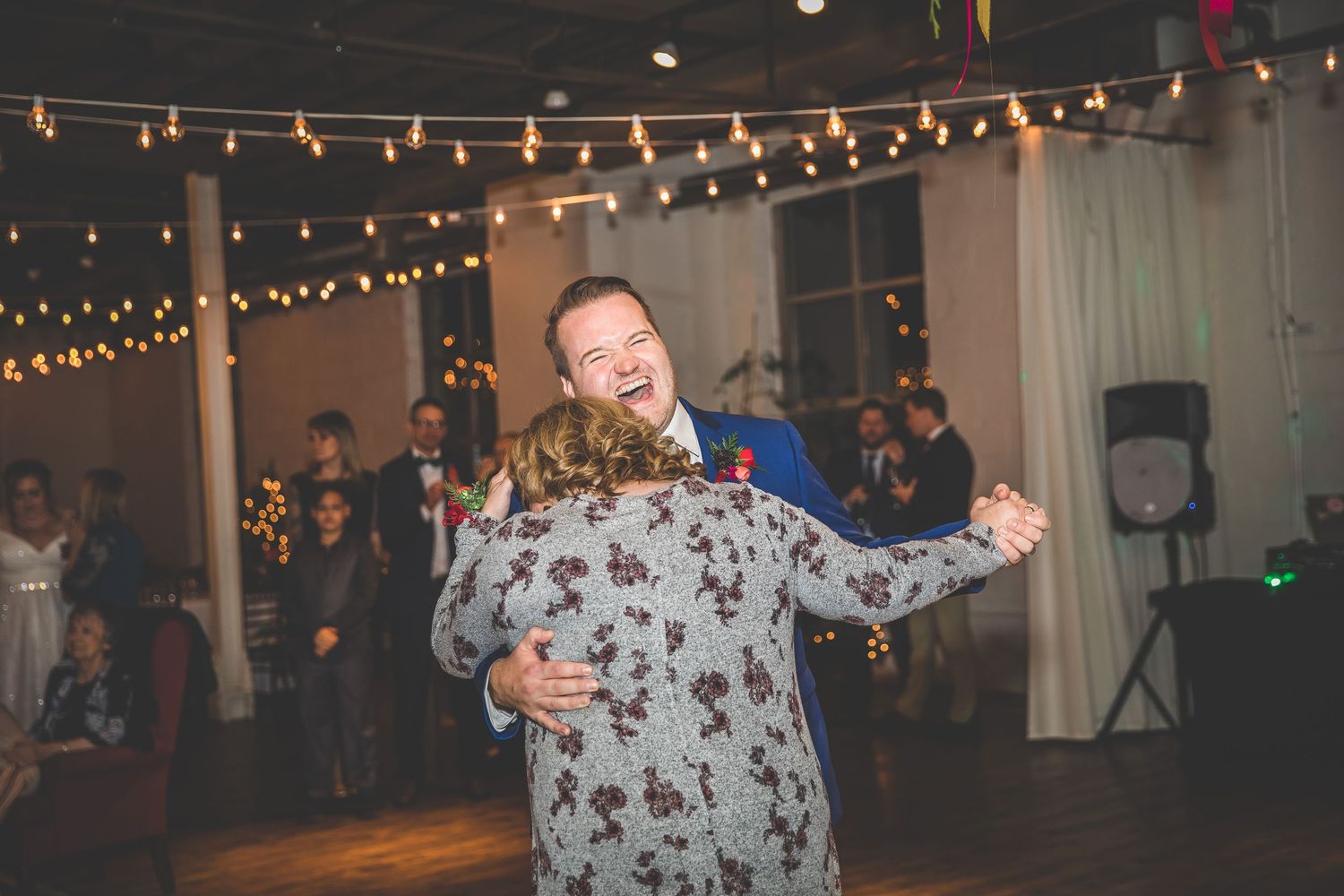 Wedding reception dance floor illuminated by overhead string lights and chandeliers.