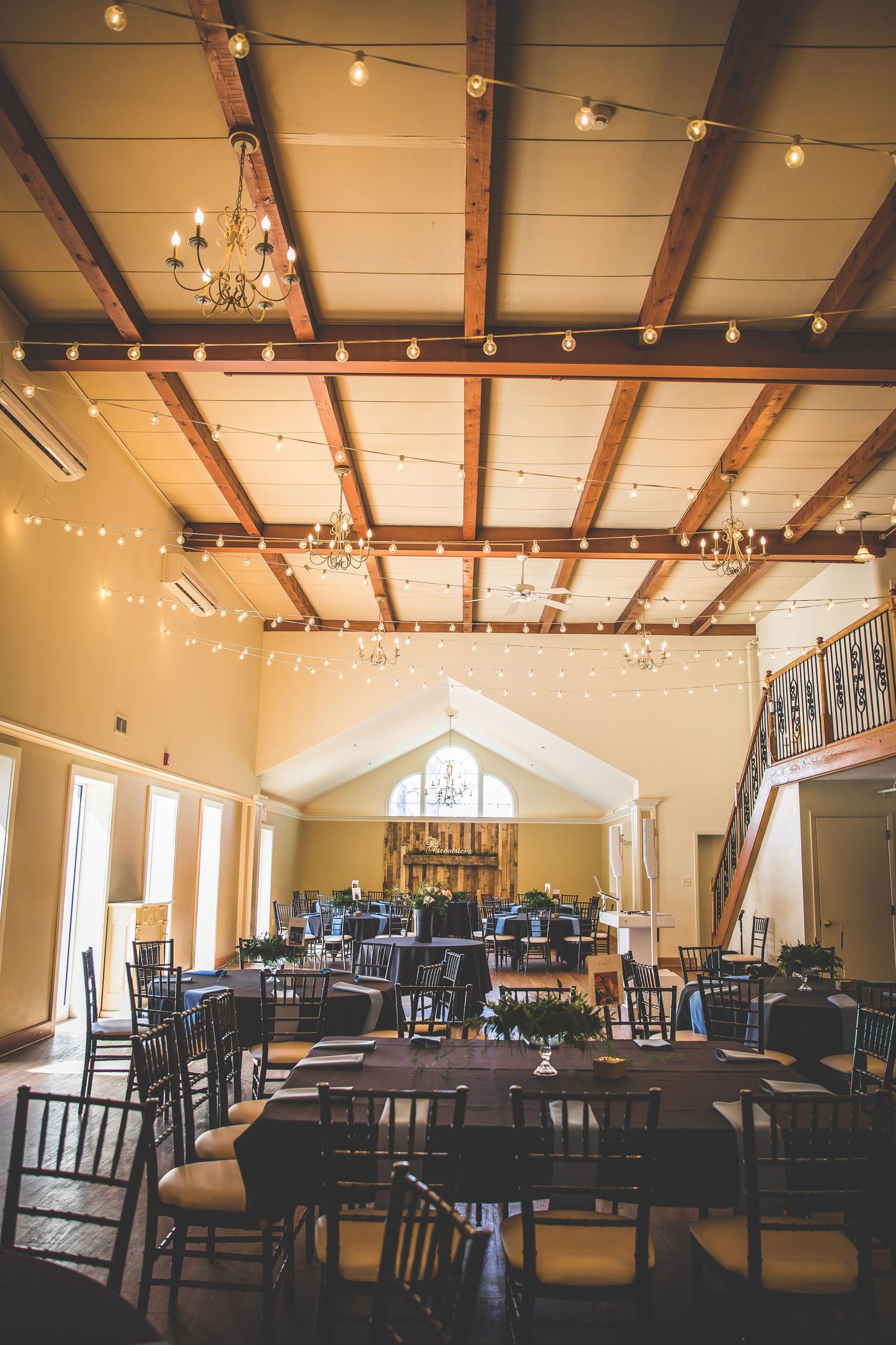 Wedding reception venue with rustic wooden beams and elegant string lights decorating the ceiling.