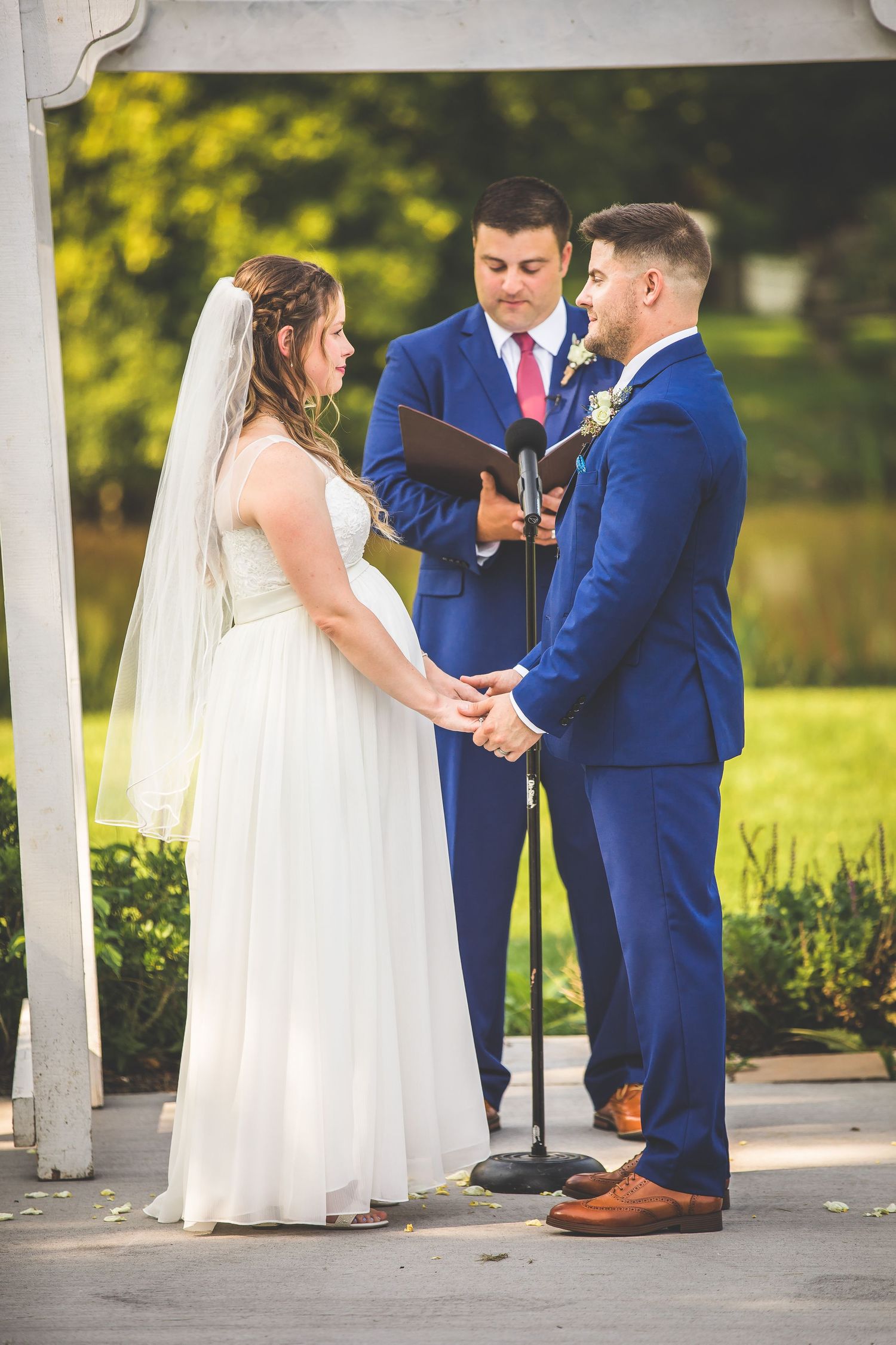 Wedding ceremony exchange taking place under an elegant white pergola with landscaped grounds.