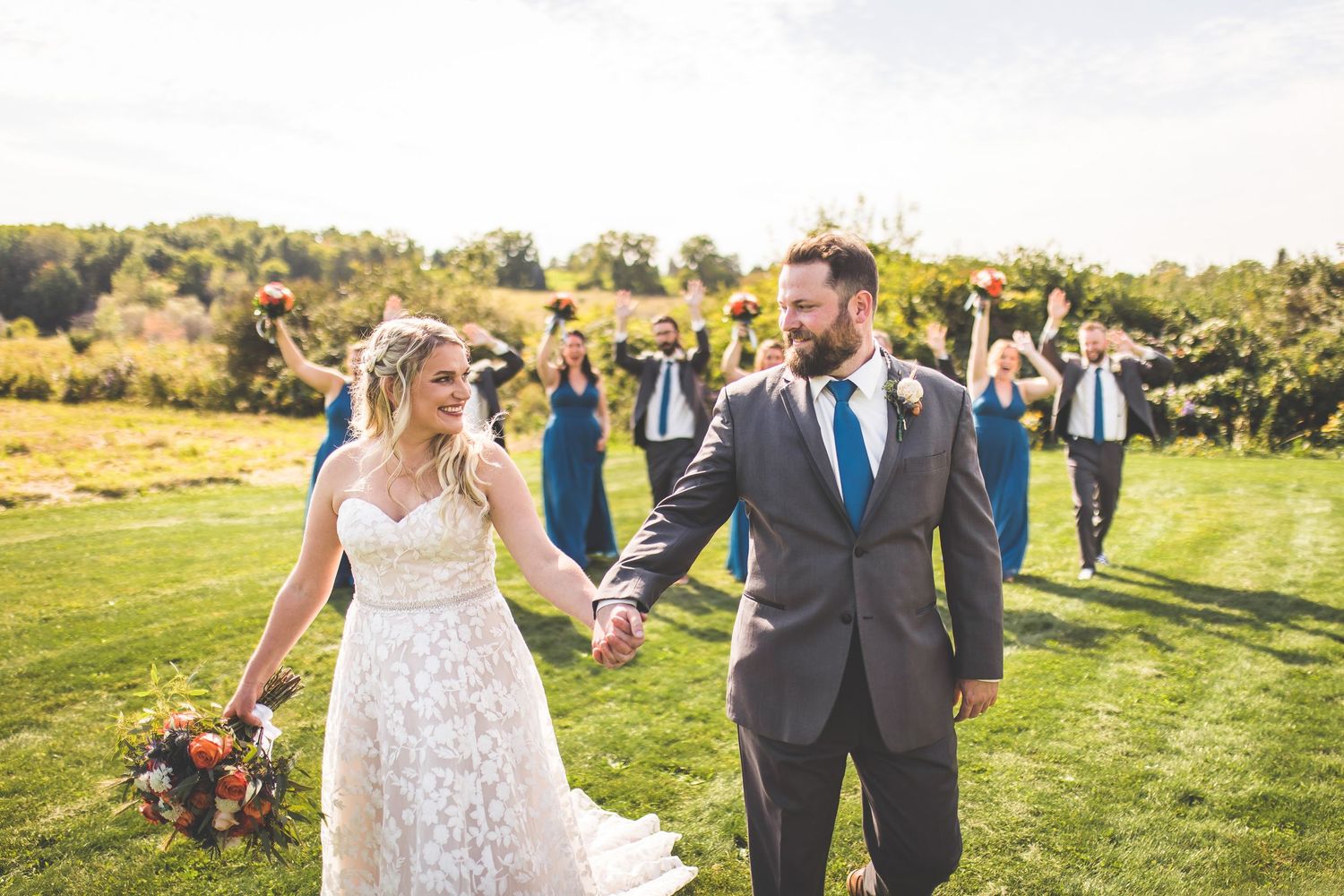 Wedding party celebrates on green hillside during golden hour.