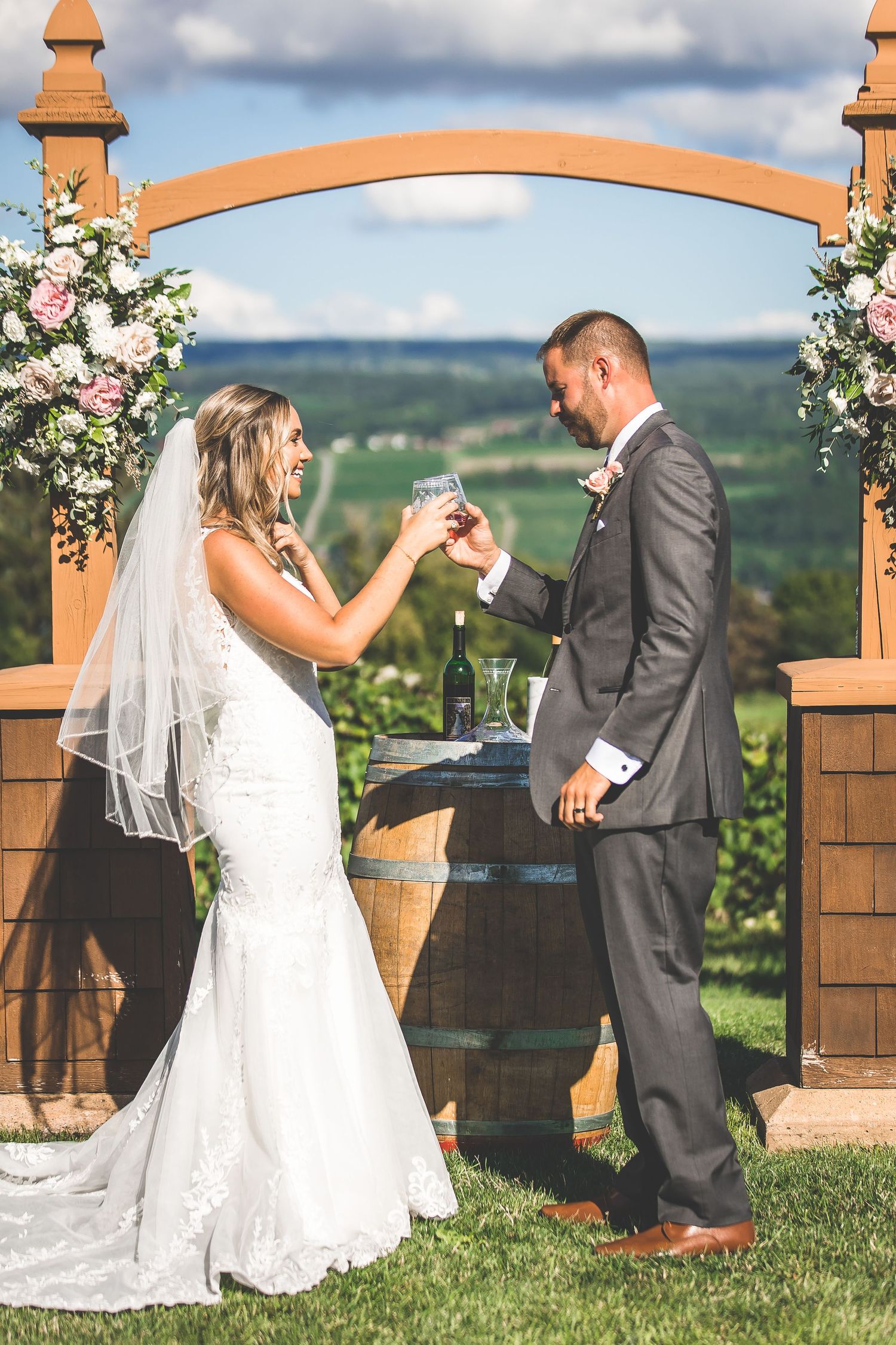 Wedding couple shares a romantic first dance moment at an outdoor vineyard ceremony with wooden archway.