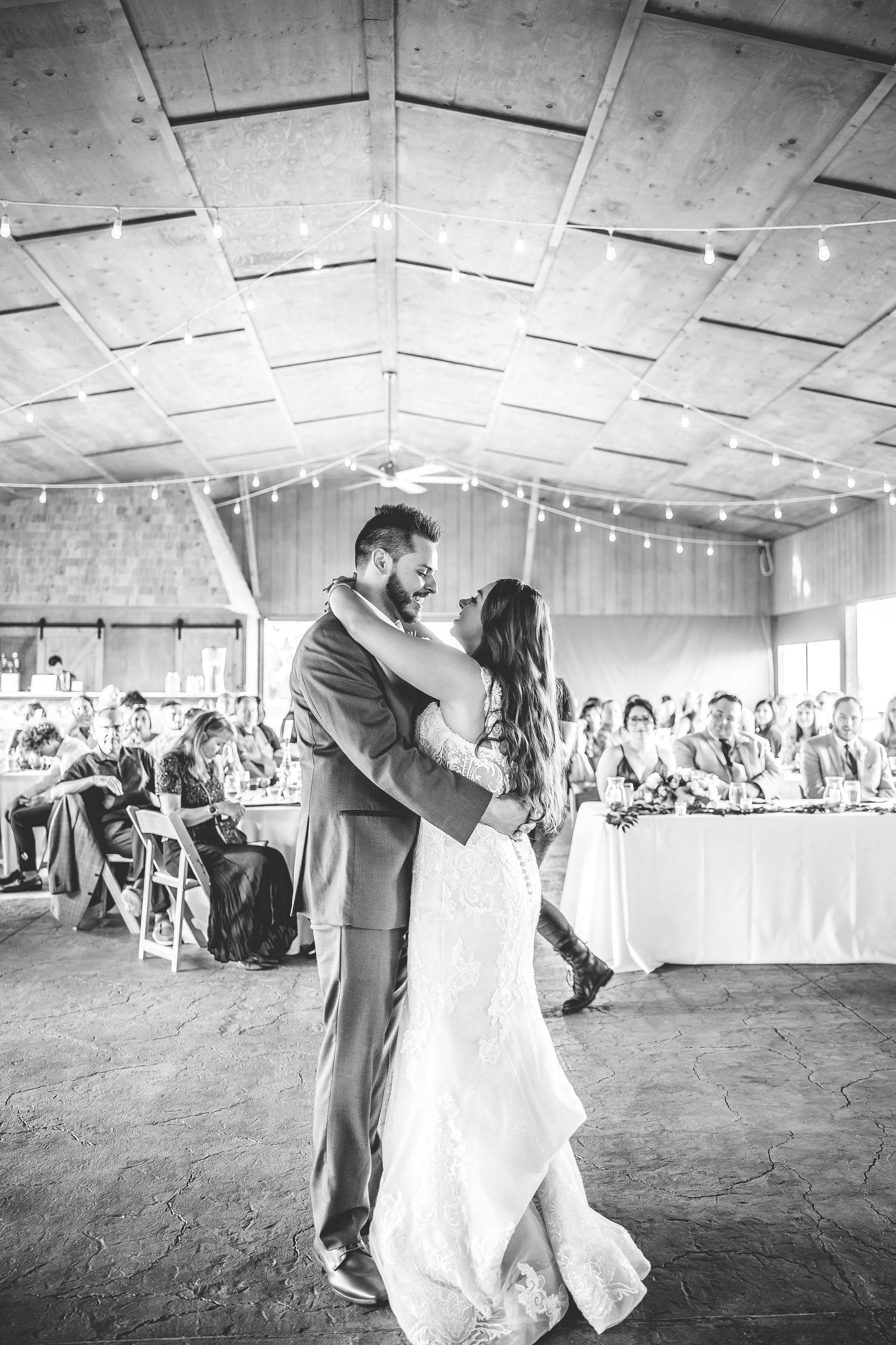 Wedding reception venue with string lights and guests seated at long tables during first dance.