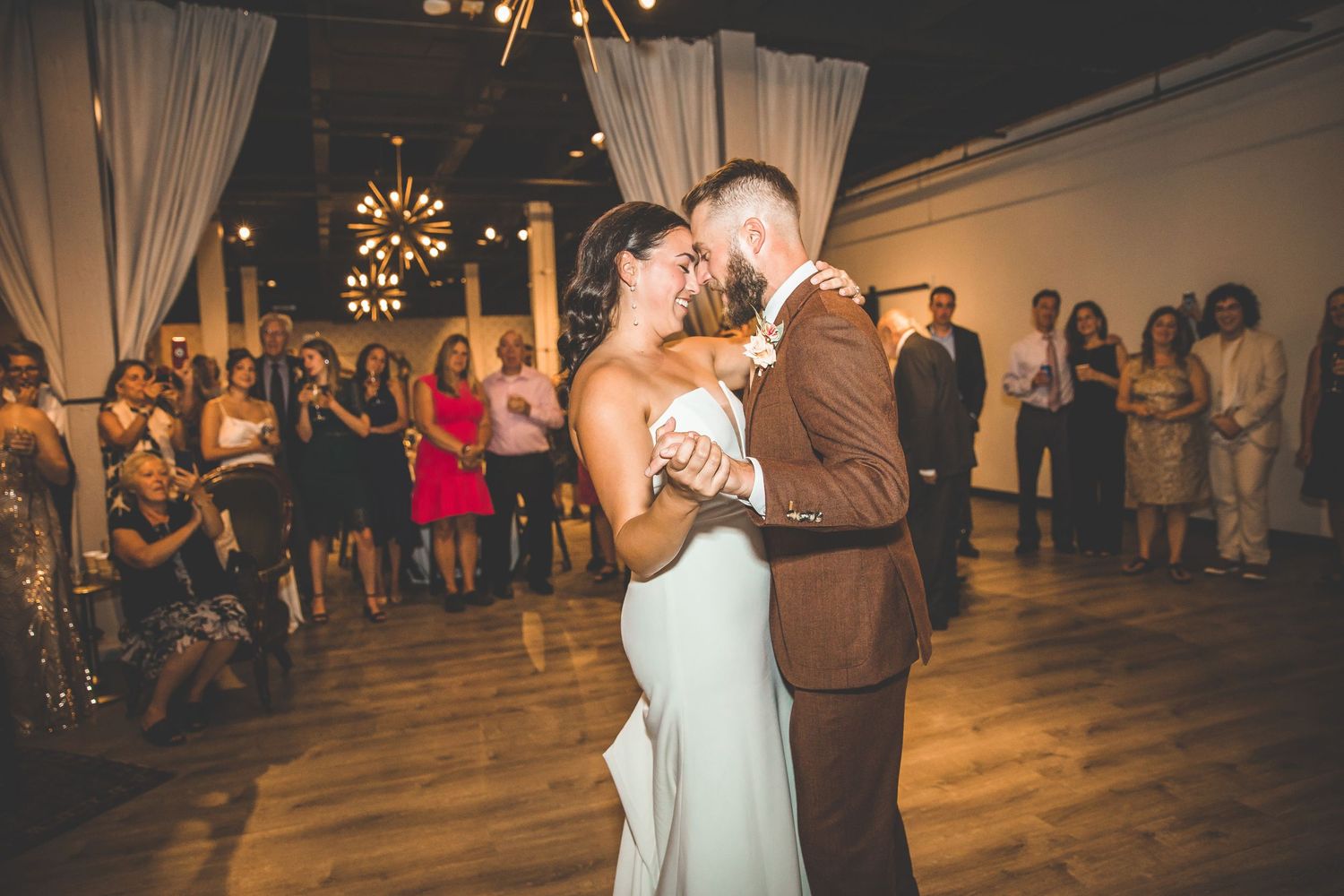 A couple shares their first dance at their wedding reception with guests watching in the background.