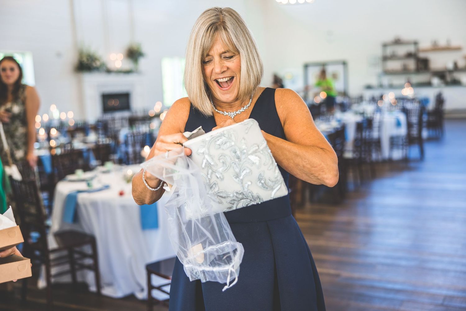 Wedding guests react with joy while opening gifts in a bright indoor venue.