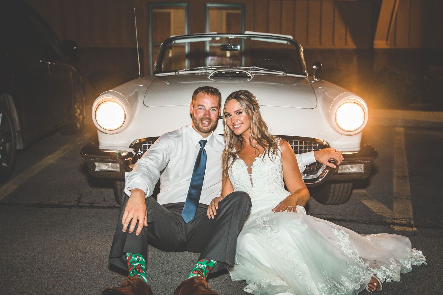 Wedding couple posing with retro car illuminated by spotlights.