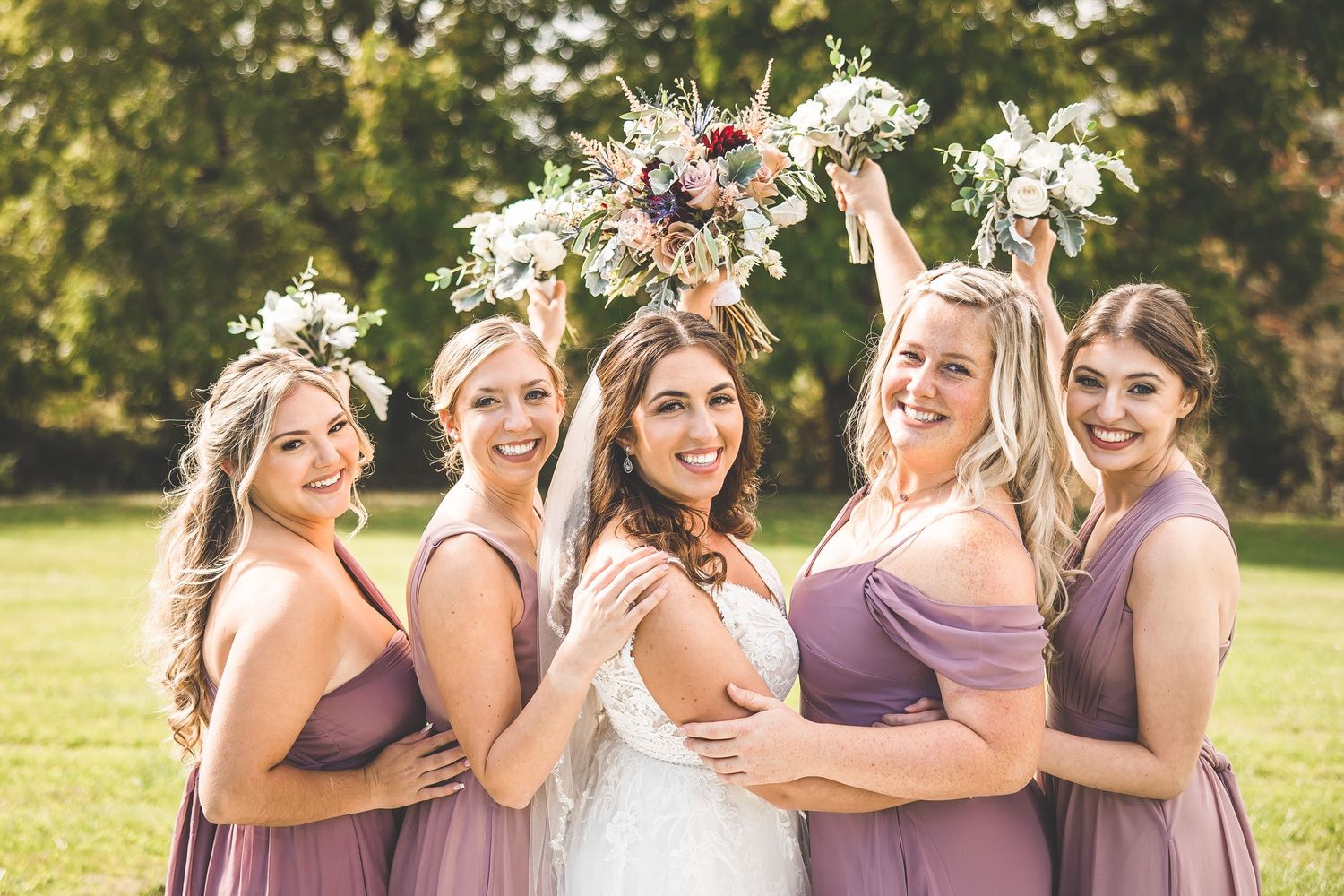 Bridal party in purple tones poses playfully with bouquets during outdoor photo session.