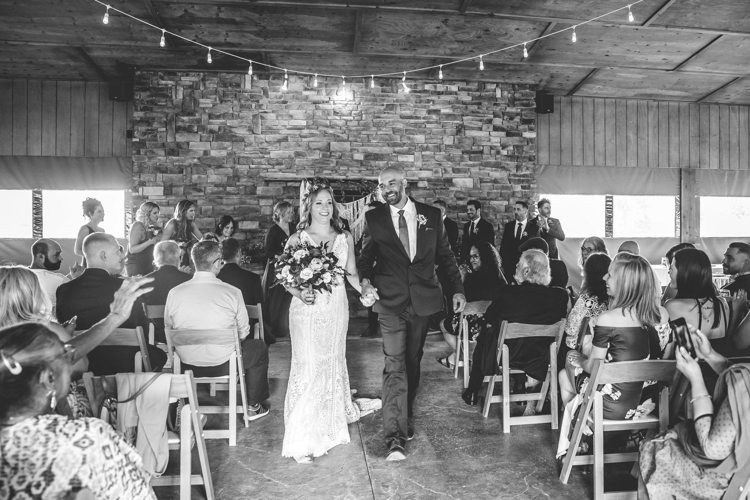Indoor wedding venue with string lights and rustic decor showing guests seated for ceremony.