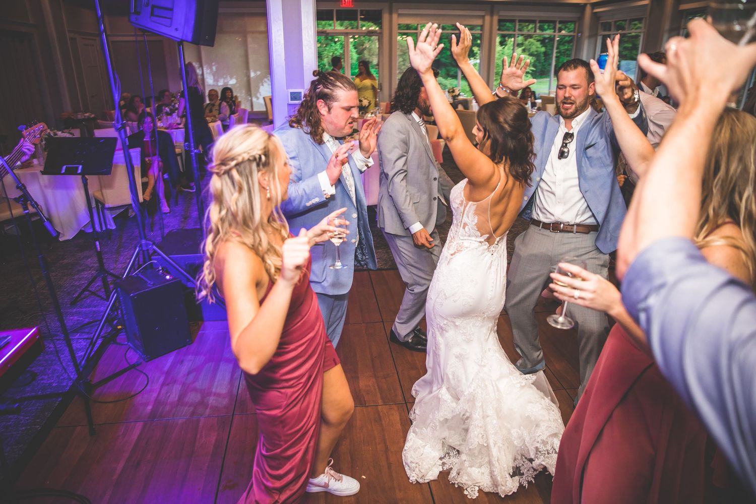 Wedding party and guests dancing under purple mood lighting in an elegant reception venue.