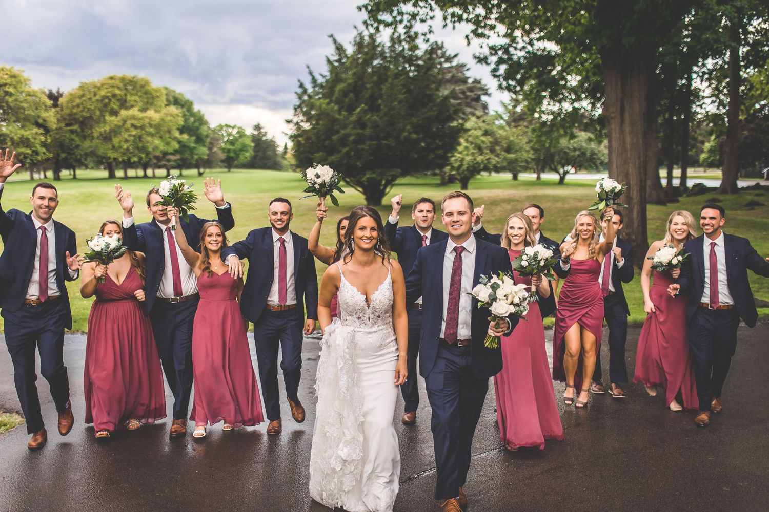 Wedding party arranged in formal group photo outdoors with burgundy and navy color scheme.
