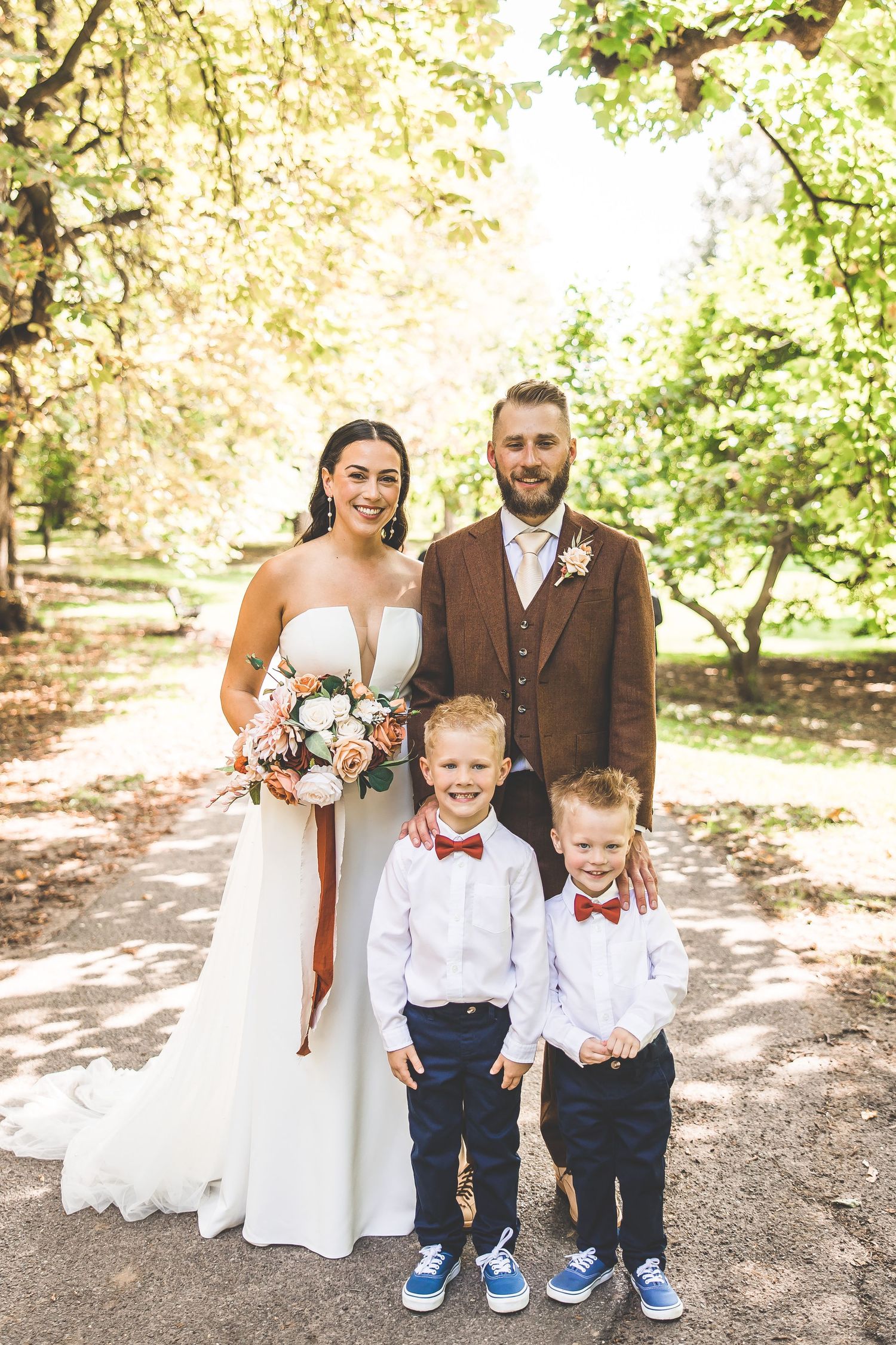 Wedding portrait with couple in brown suit and white dress with two young boys in bow ties.
