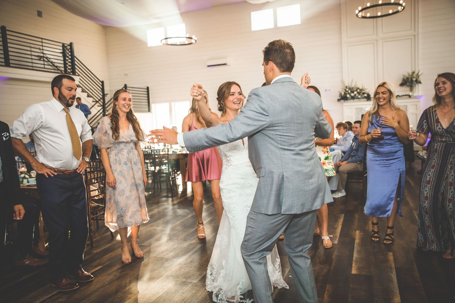 Wedding guests dancing and celebrating on a wooden dance floor at an indoor reception.