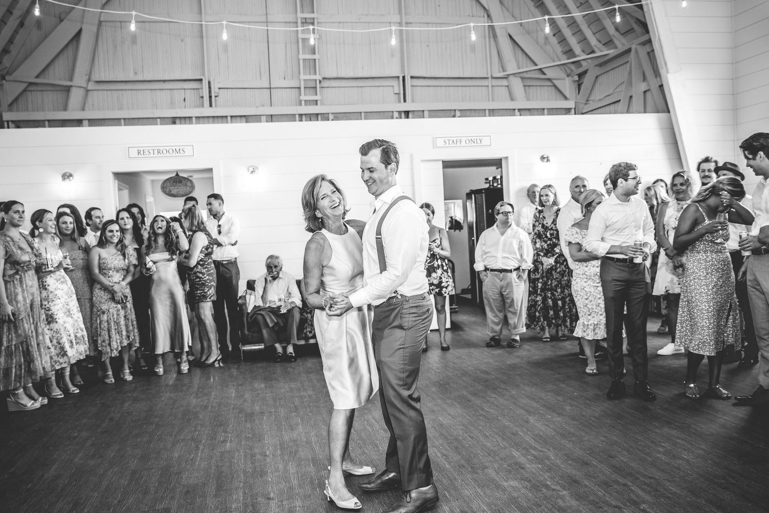 Black and white photo of wedding guests watching a couple dance in a spacious reception hall.