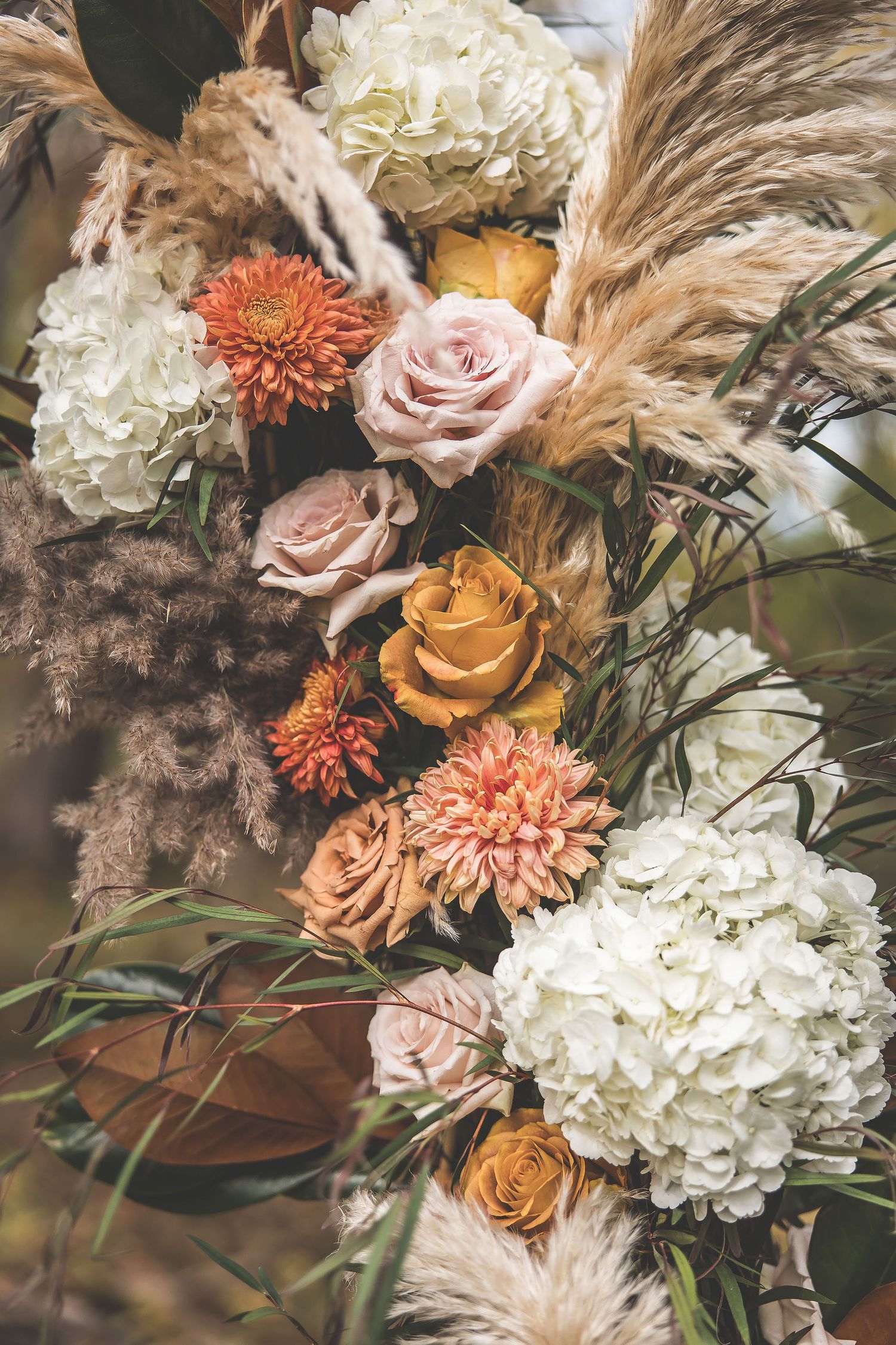 Romantic wedding floral arrangement with pampas grass, roses, and hydrangeas in coral and cream tones.