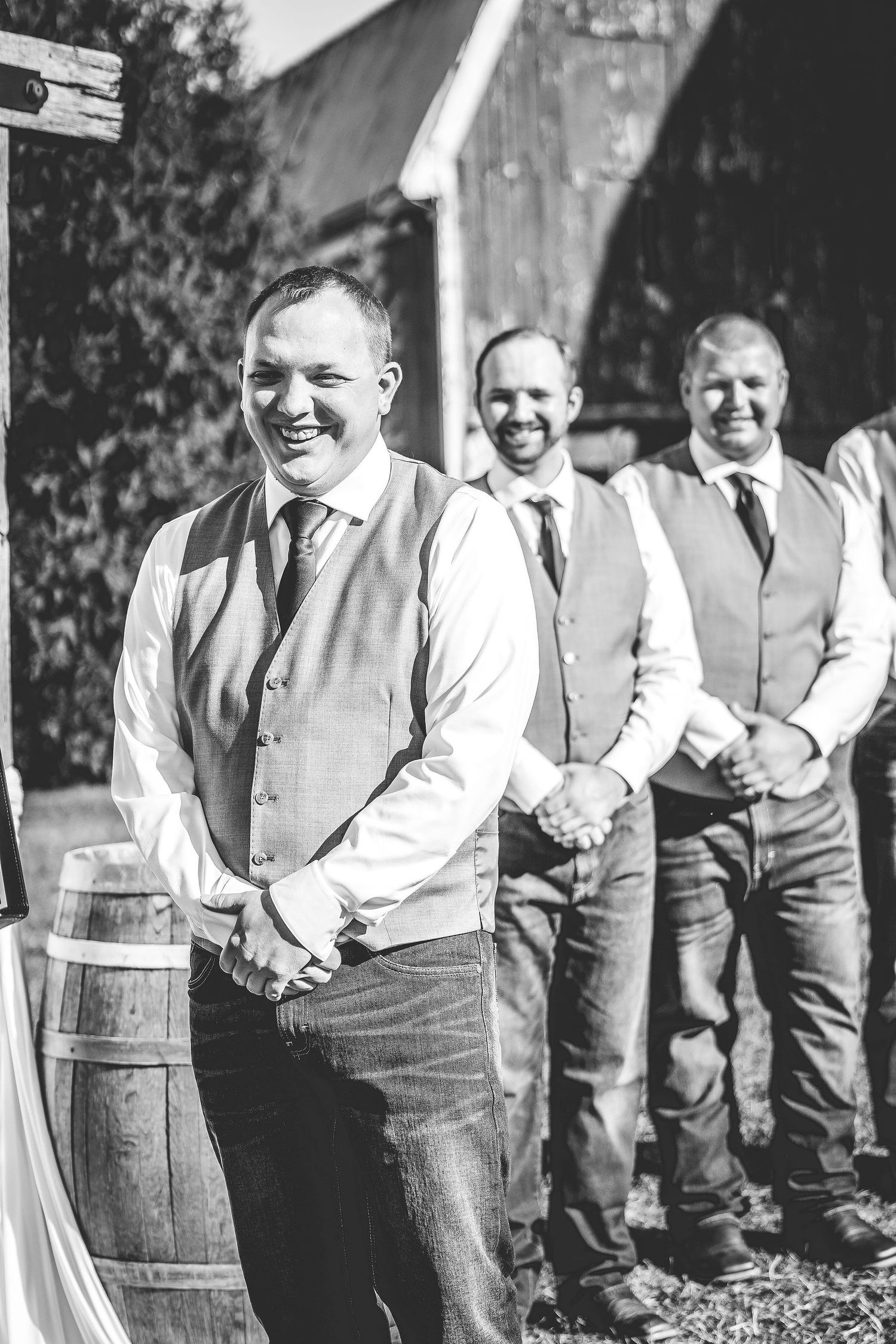 Wedding party members in casual attire pose with rustic wooden barrels.