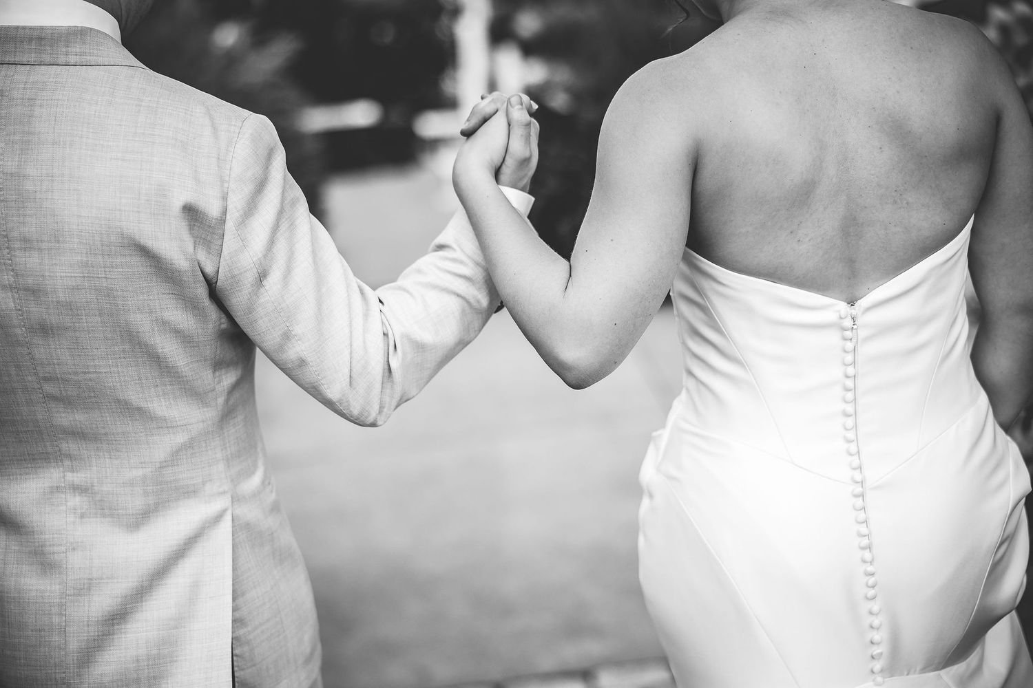 Black and white close-up of a couple's joined hands showing wedding attire details.