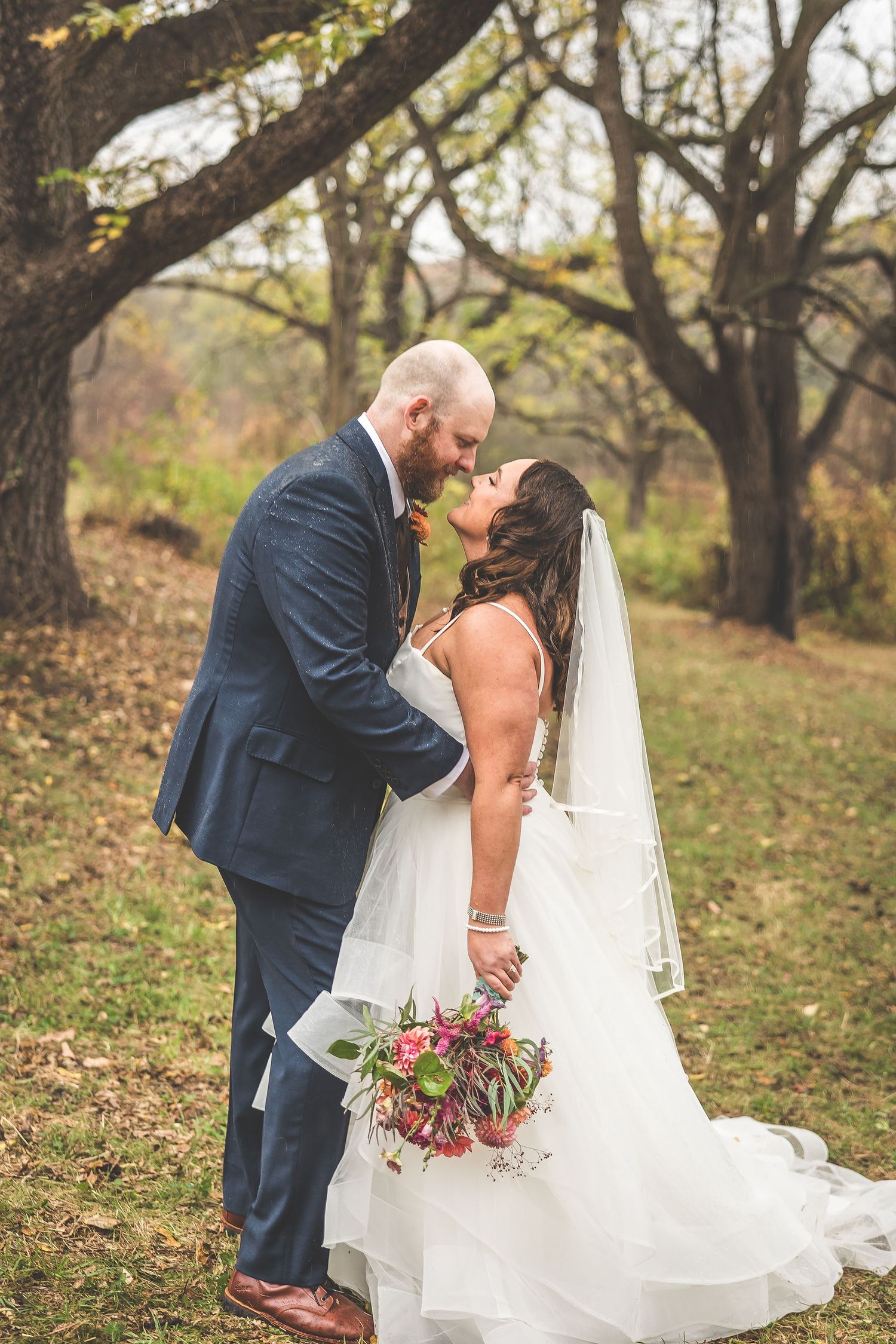 Romantic wedding couple shares tender moments in an autumn forest setting with fallen leaves.