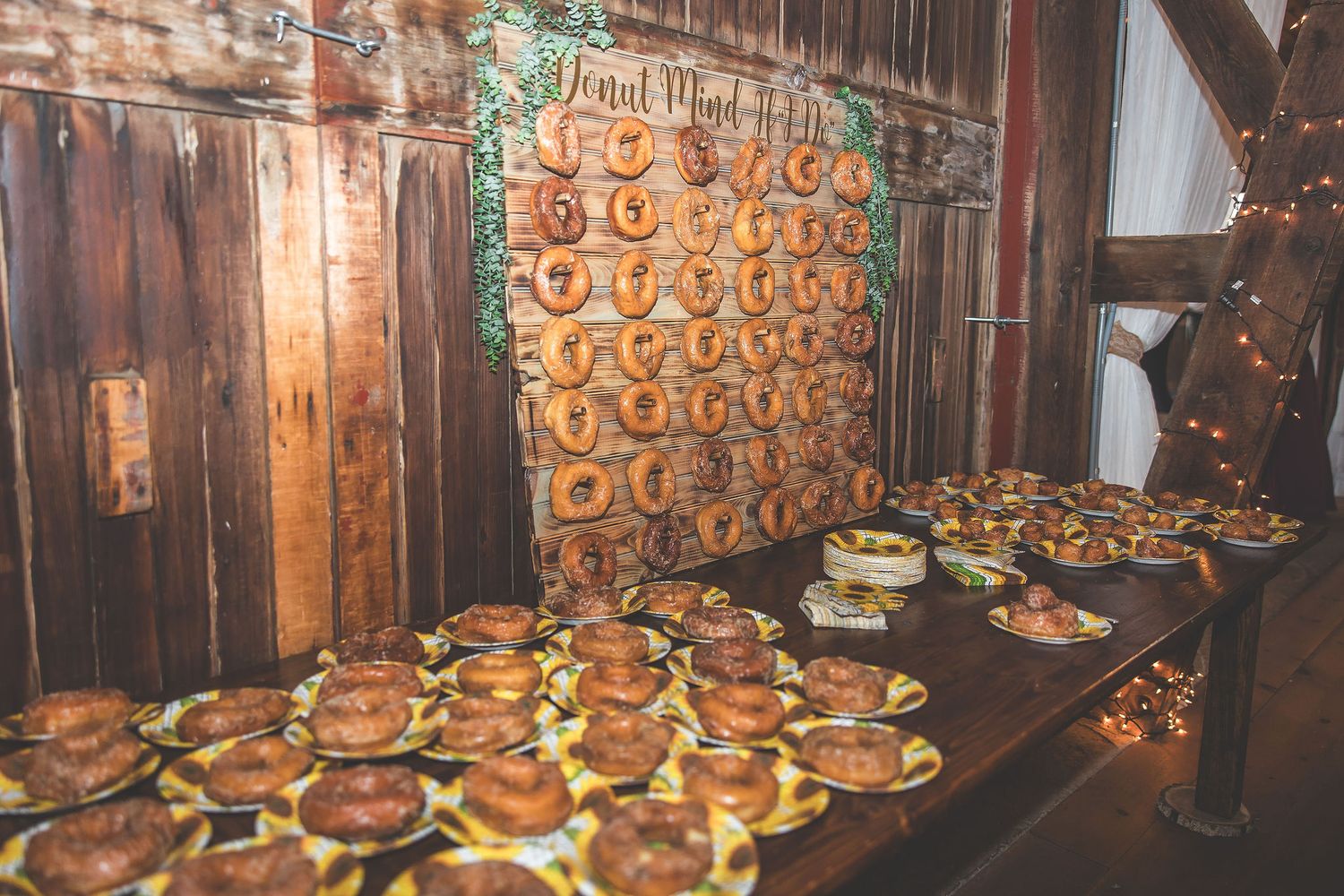 Rustic wedding dessert table with rows of donuts displayed on wooden wall backdrop.