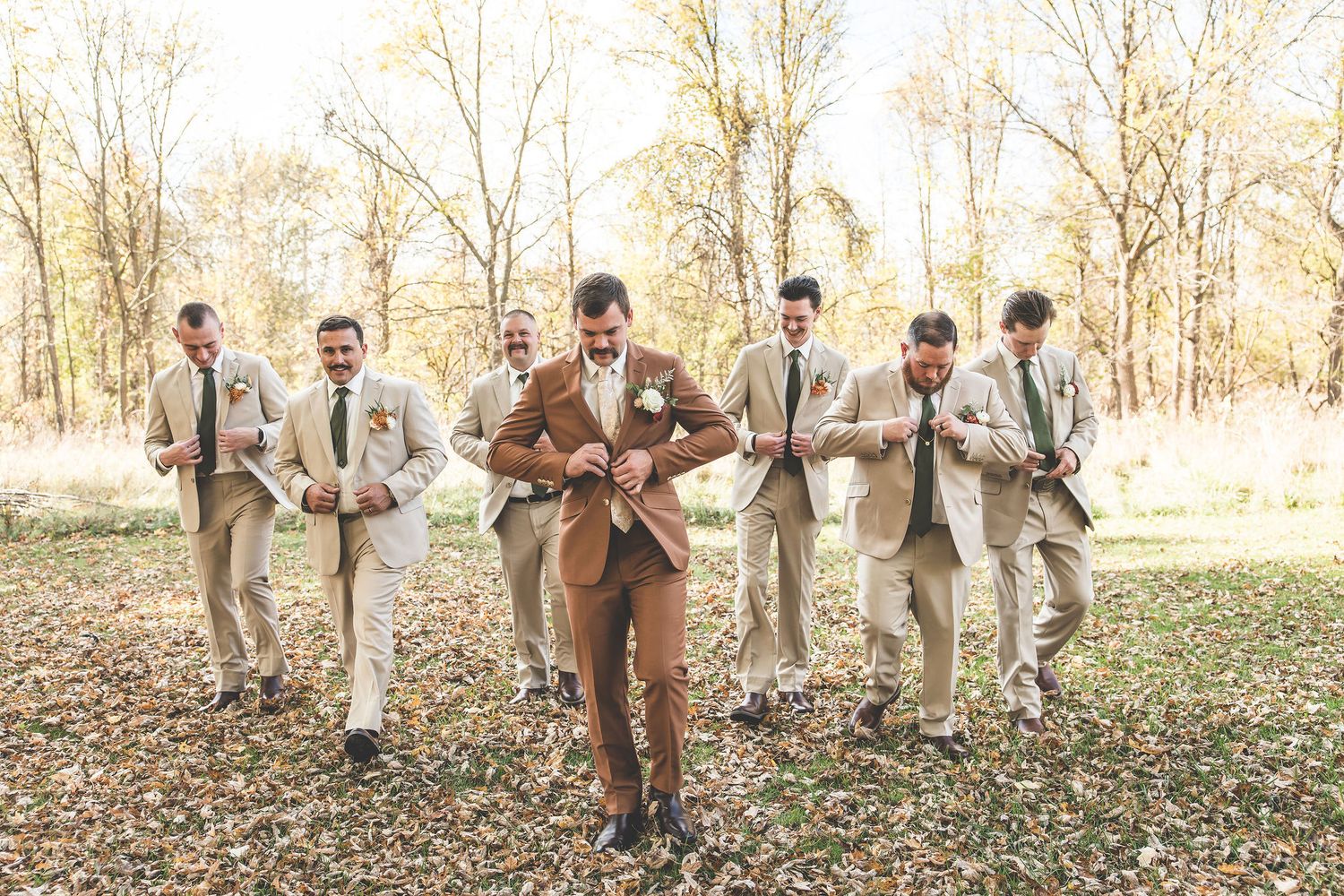 Wedding party runs playfully through fallen leaves in an autumn forest setting.