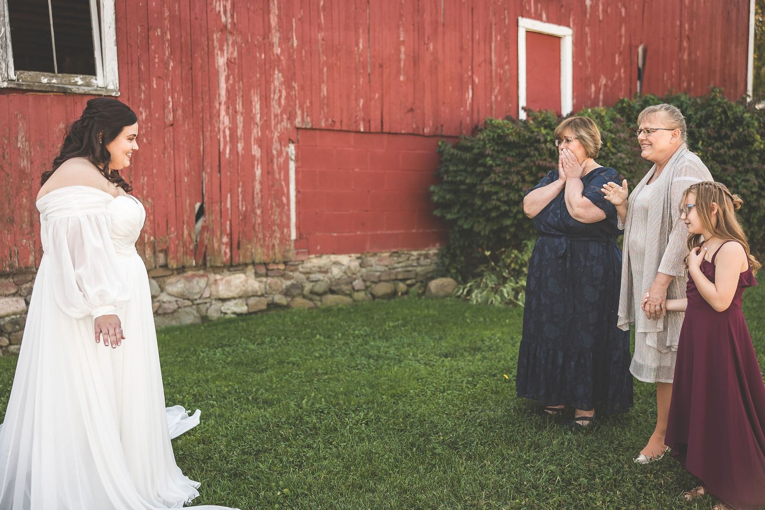 Wedding party members gather outside a red barn for photos.