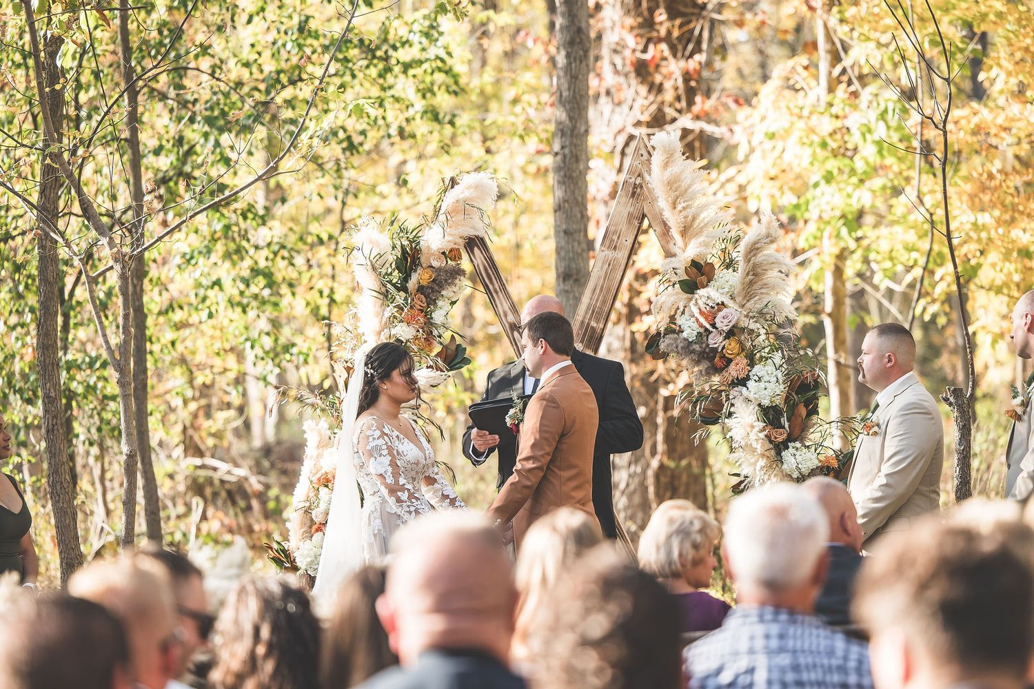 Wedding guests seated in rows at an outdoor autumn ceremony among trees.