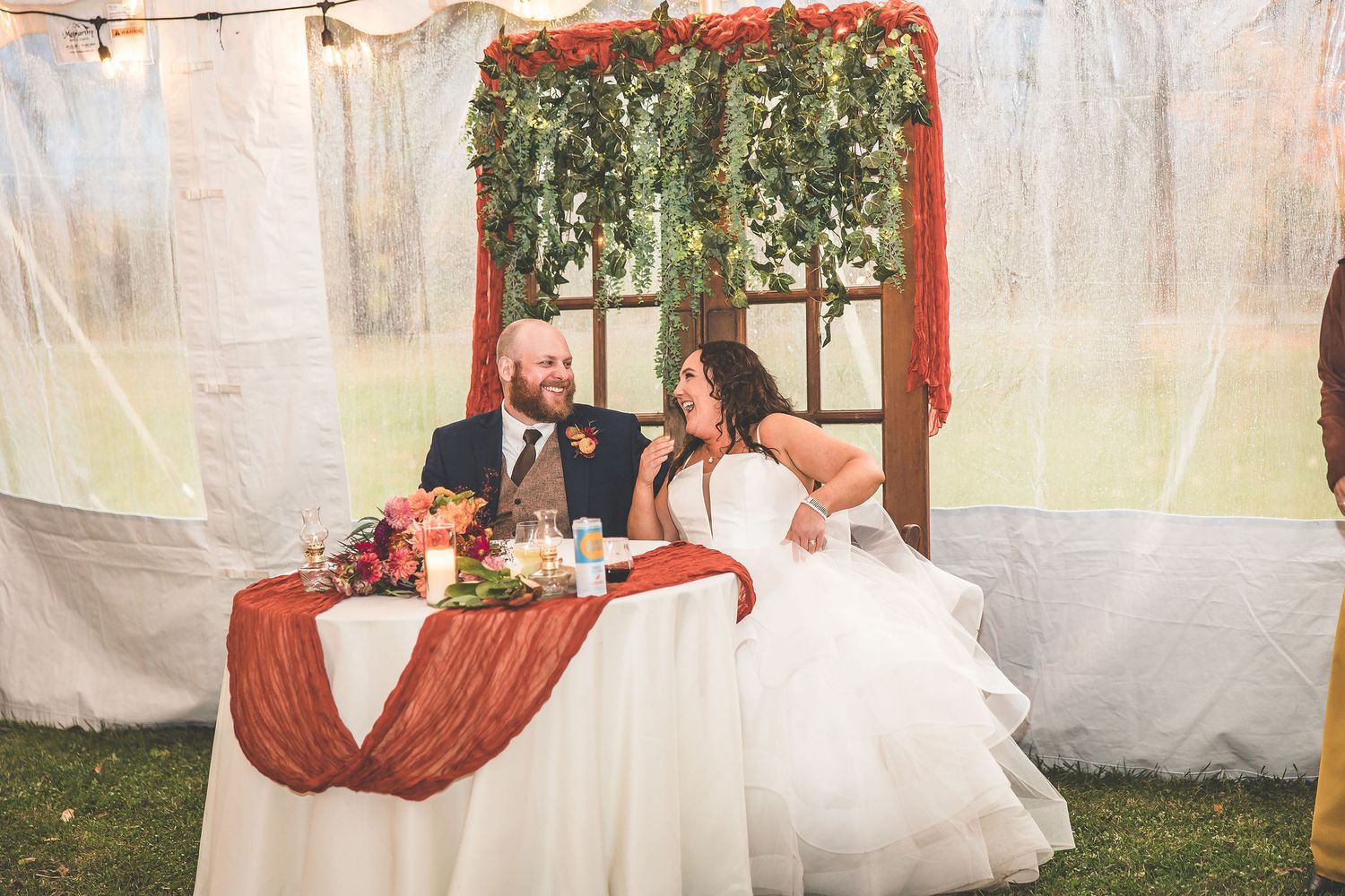 Wedding tent decorated with string lights and flowing white fabric for evening celebration.