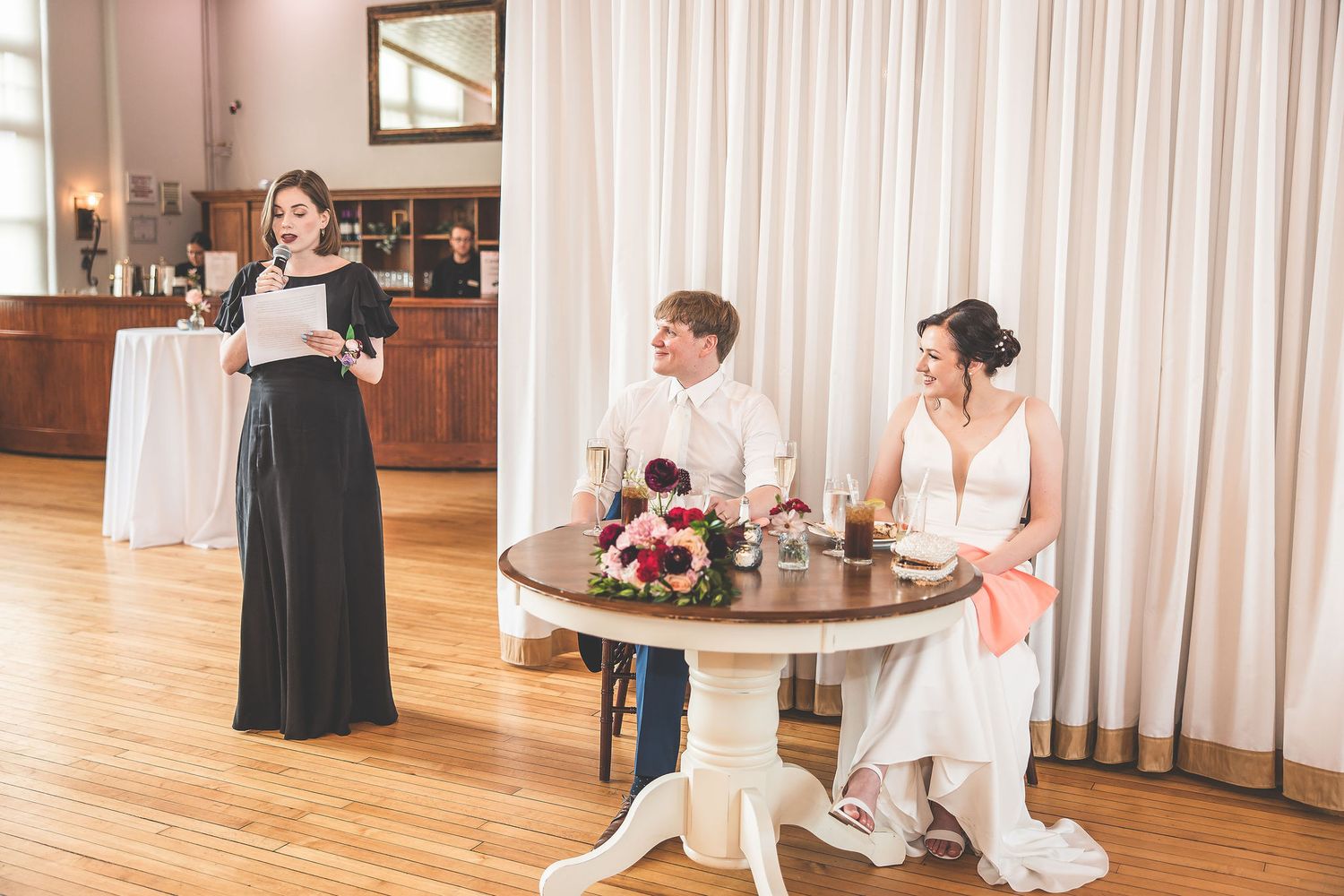 Wedding reception setup in a bright room with white curtains and wooden accents.