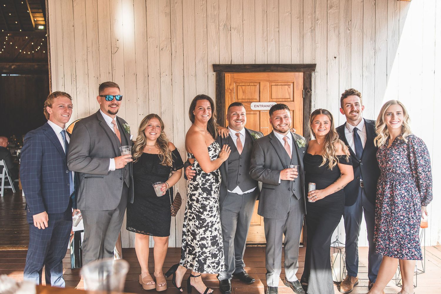 Wedding party lineup poses inside rustic barn venue with wooden walls and ambient lighting.