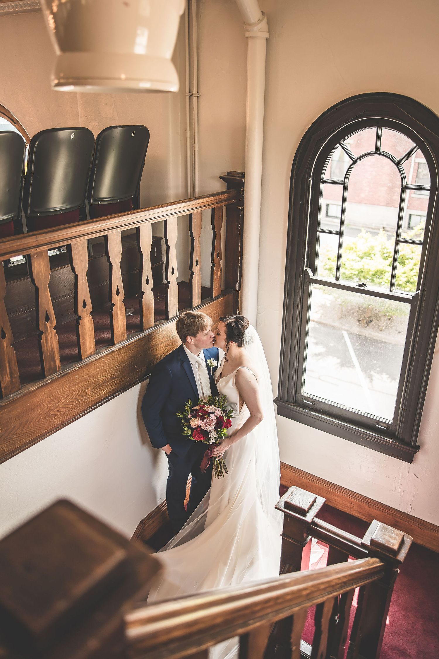 Wedding photography session in a historic theater featuring wooden railings and arched windows.