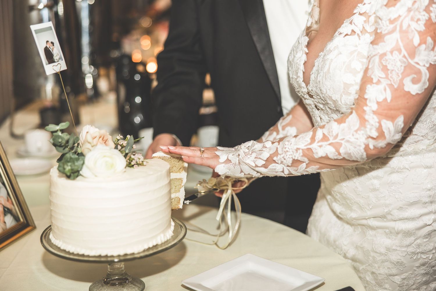 Close-up view of newlyweds cutting their three-tiered white wedding cake.