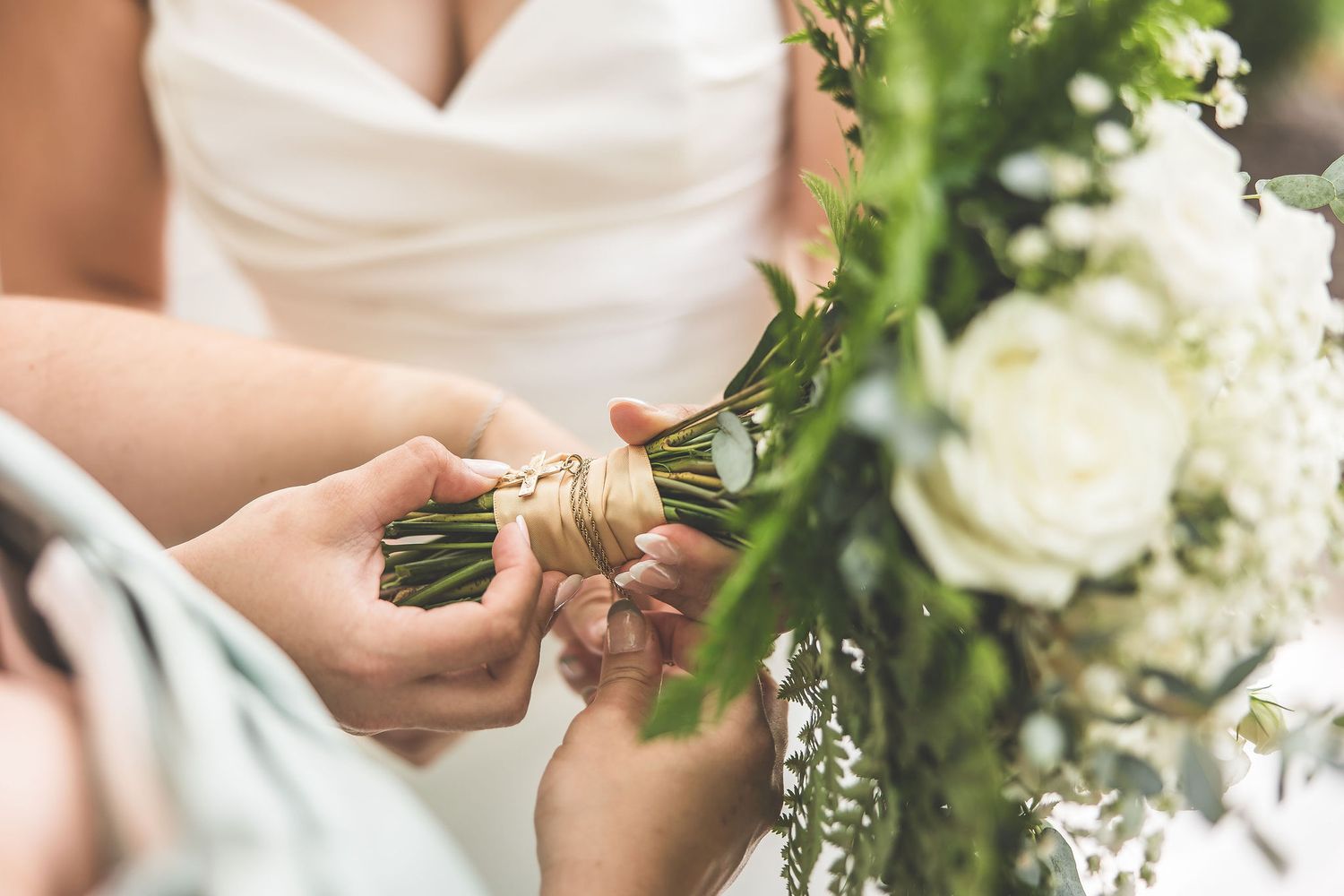 Close-up details of white floral bouquets and sage green bridesmaid dresses at an outdoor wedding.