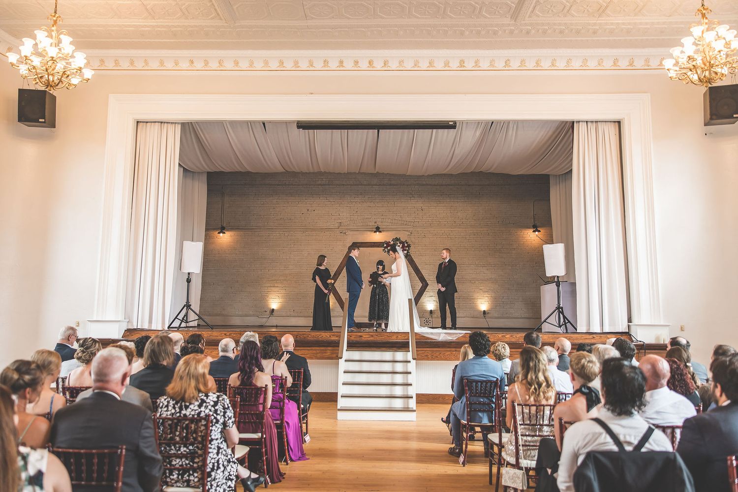 Elegant wedding venue with chandeliers and white walls features rows of chairs set up for a ceremony.